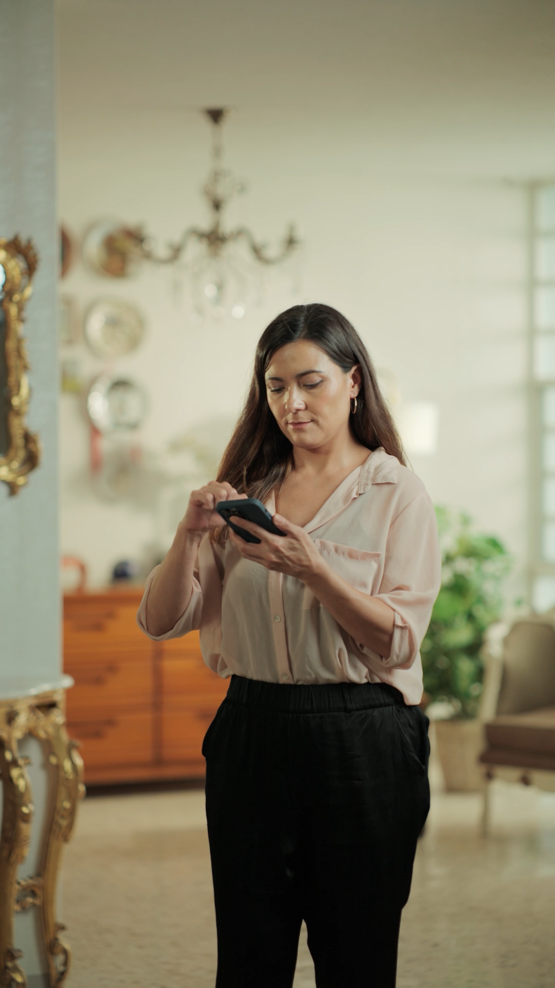 Woman in pink blouse using smartphone in elegantly decorated living room.