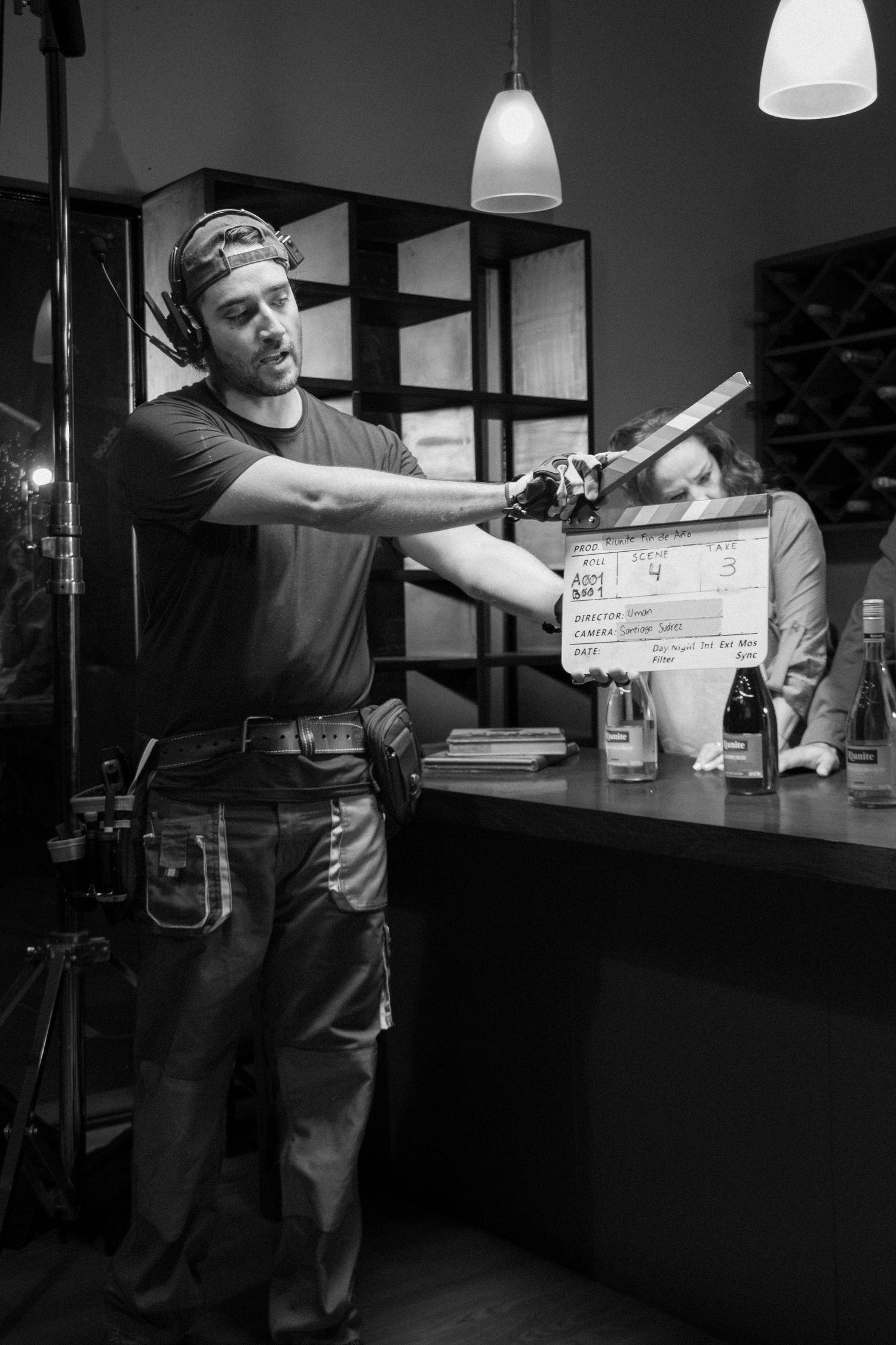 Male crew member holds clapperboard on a dimly lit professional film production set in black and white.