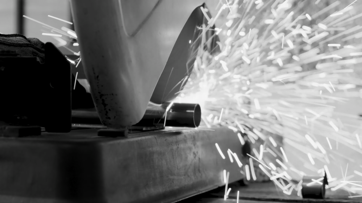 Black and white close-up of angle grinder cutting metal with bright sparks flying.