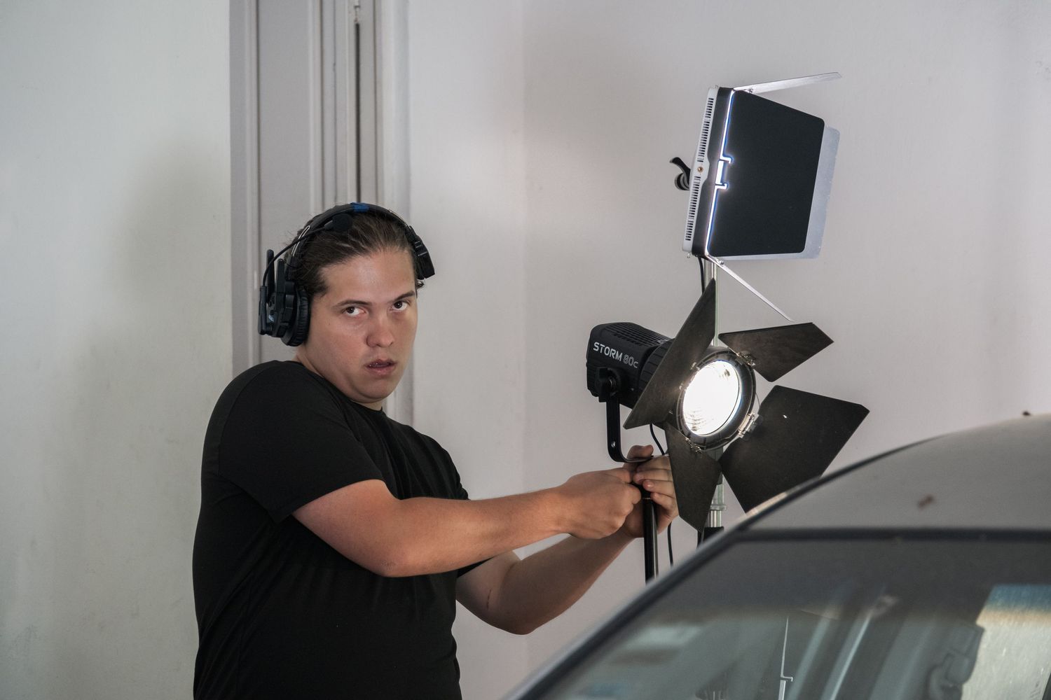 A man wearing headphones adjusts professional lighting equipment on a film or video production set.