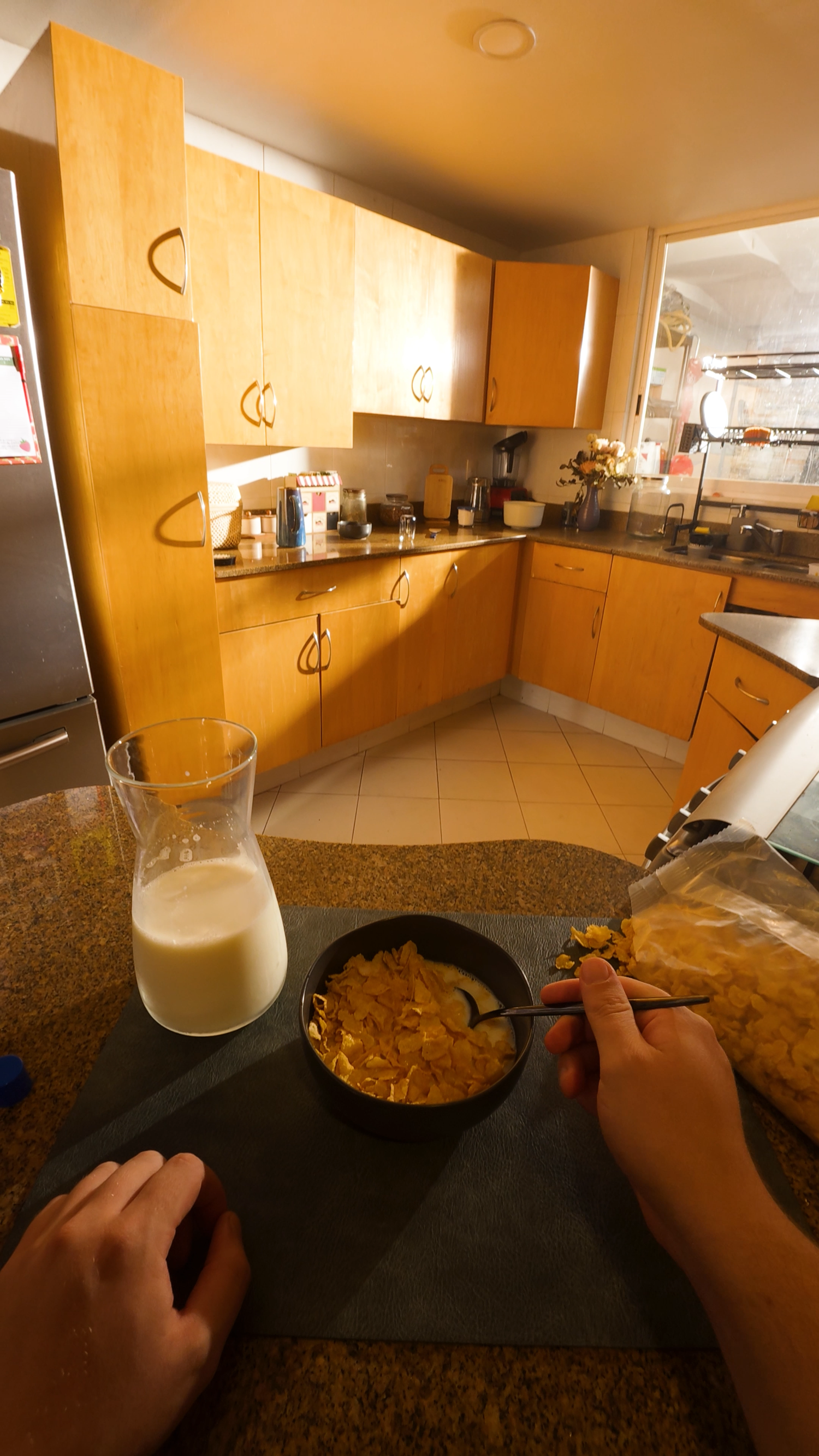 POV shot of person eating cereal with milk jug on granite counter in yellow kitchen.