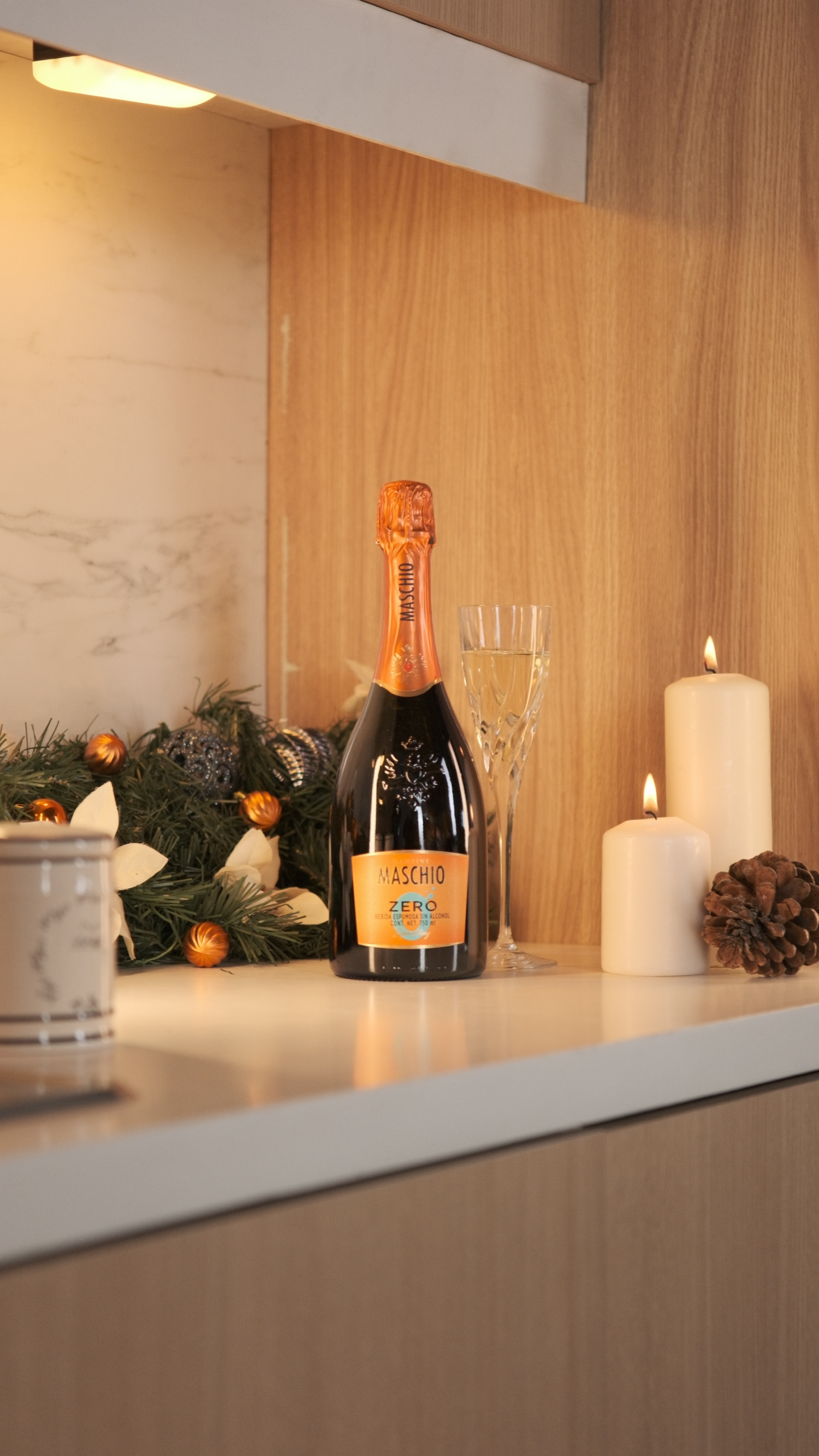 Maschio Zero sparkling wine bottle displayed with candles and Christmas greenery on a wooden kitchen counter.