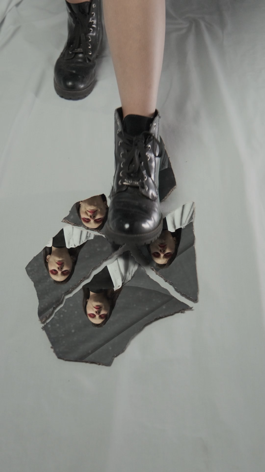 Black lace-up boots stepping on torn paper revealing multiple small faces peeking through holes.