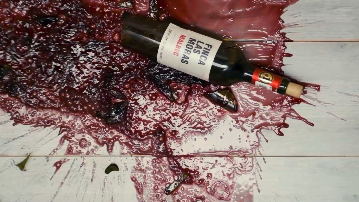 Red wine bottle spilled on white surface with wine splattered around it dramatically.
