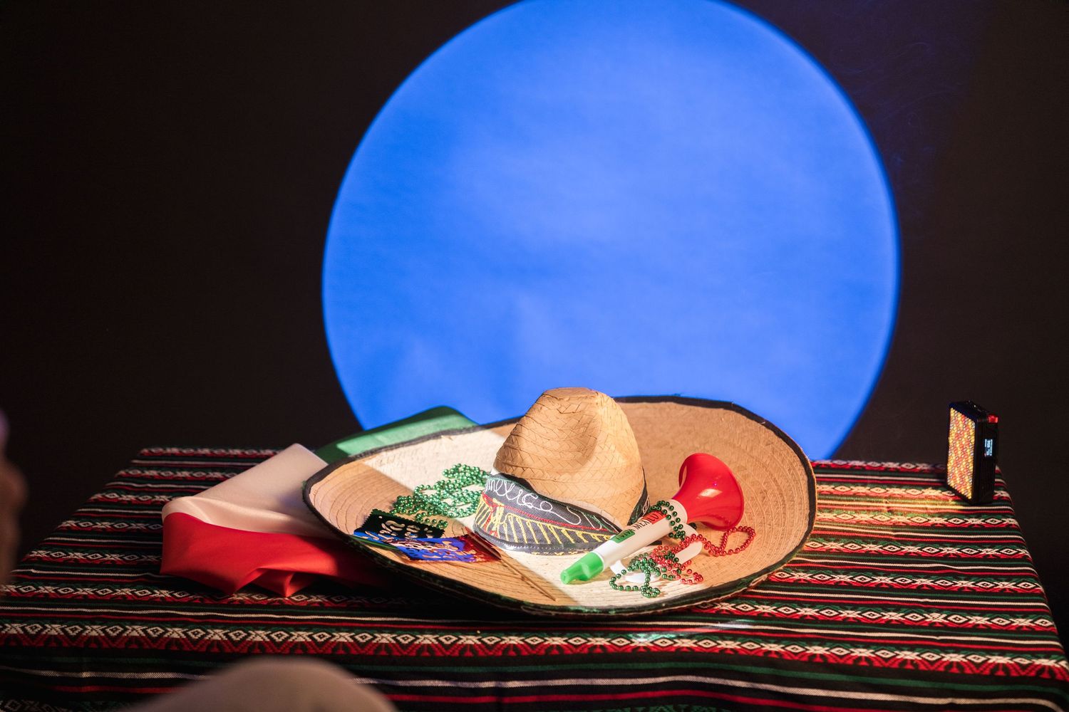 Traditional Mexican sombrero and colorful props arranged on a striped textile under blue light.