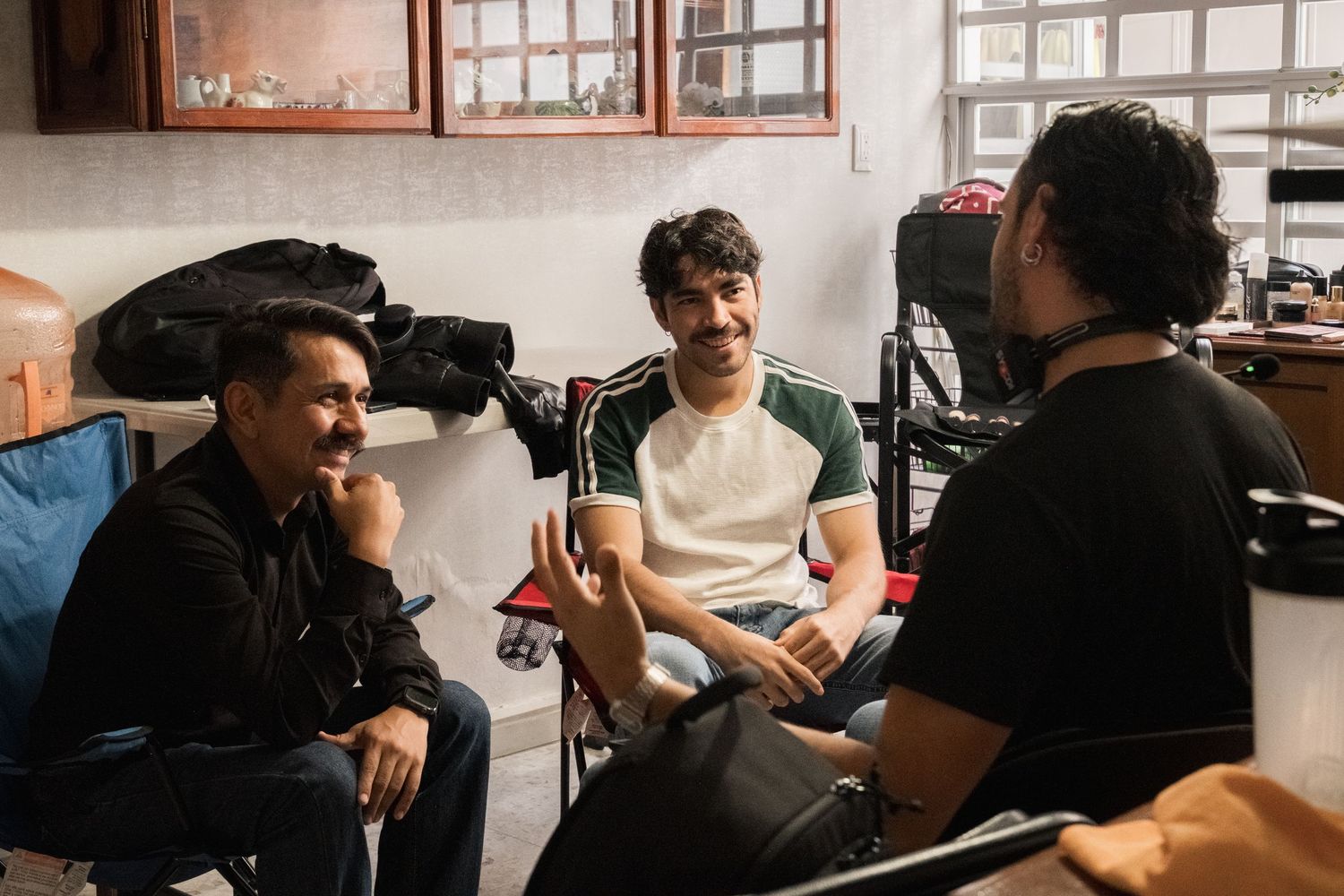 Three male cast and crew members relax and chat between takes on film set.