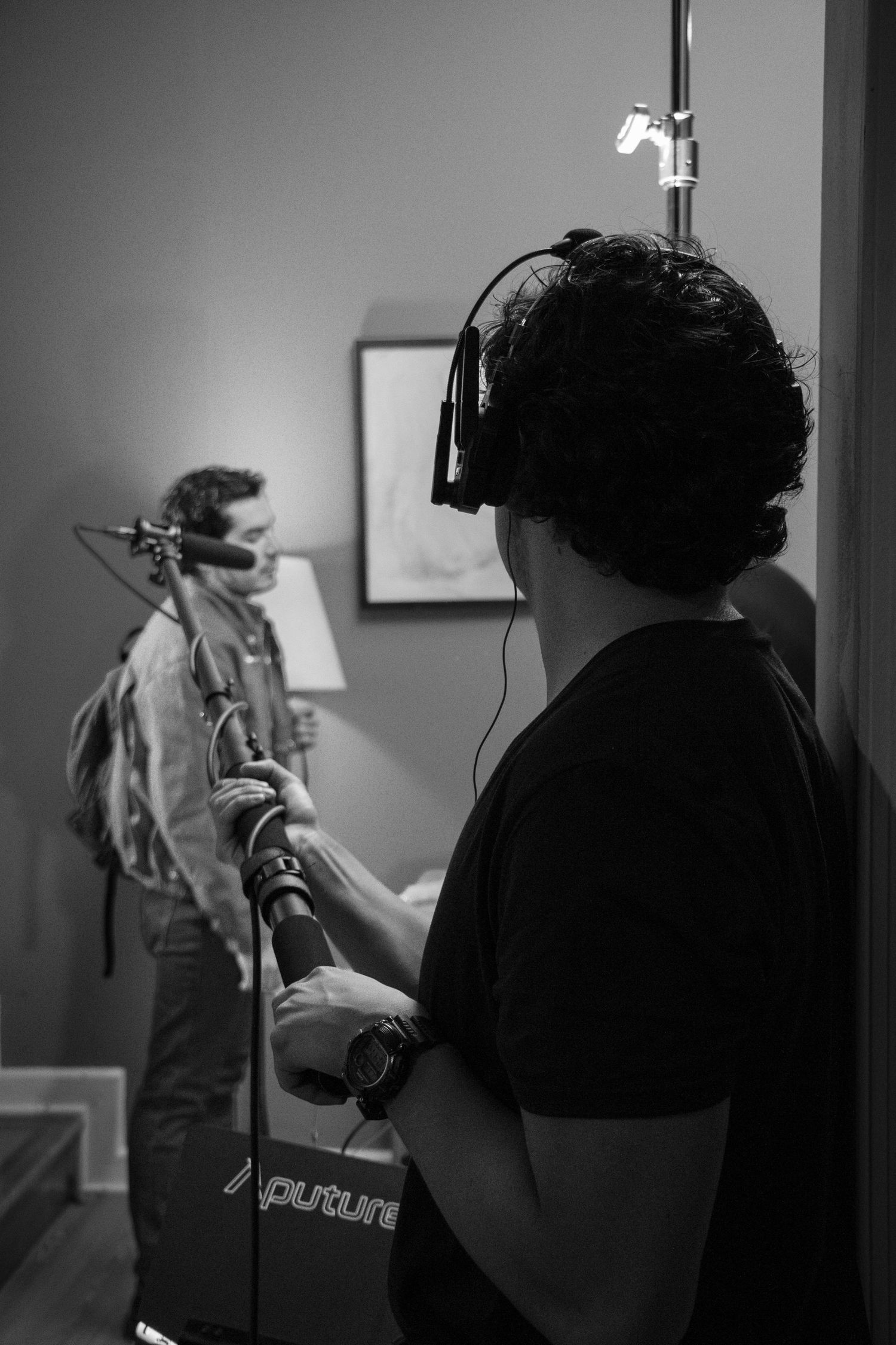 Sound technician wearing headphones operates boom mic on film set in black and white photography.