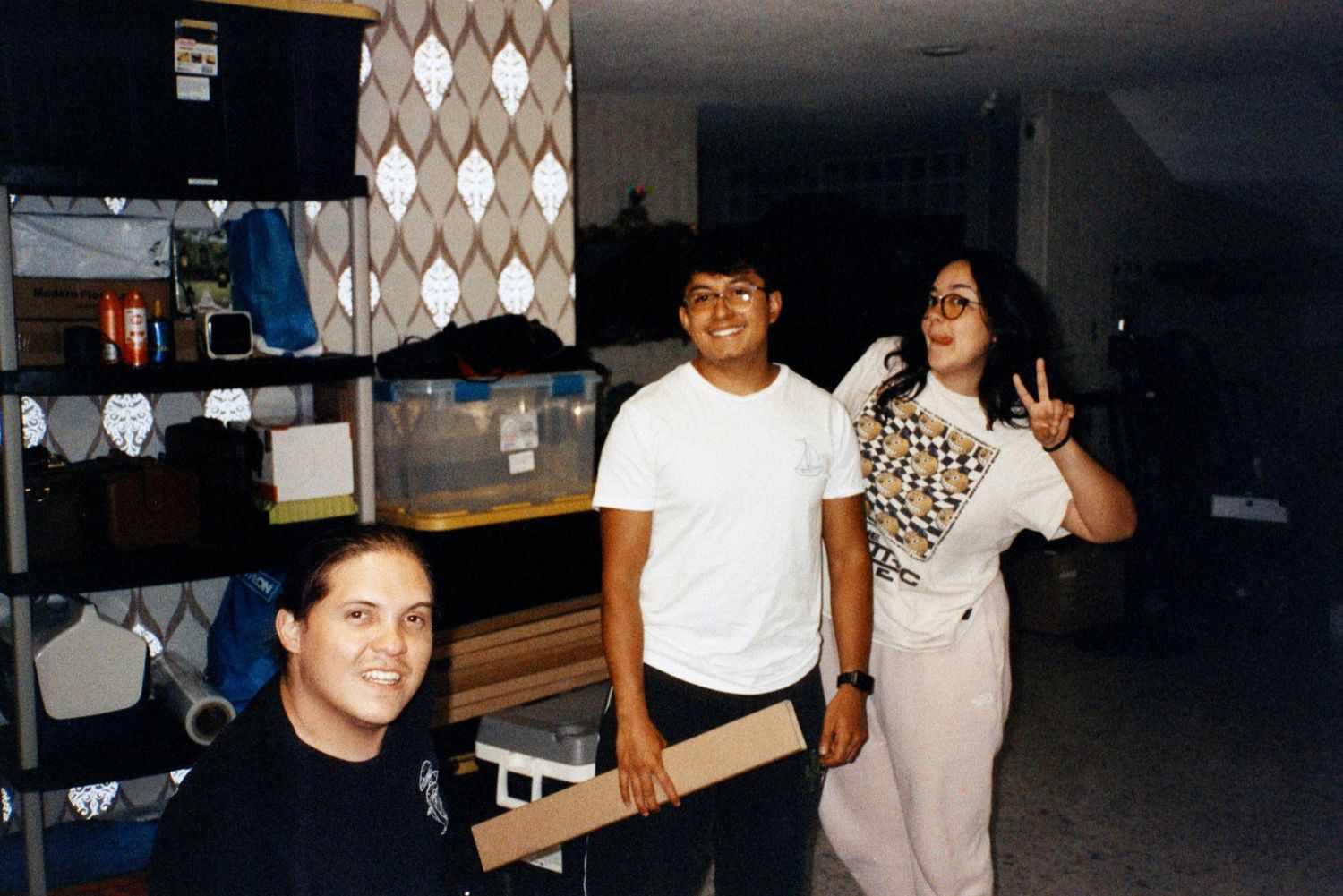 Three crew members pose and smile in a storage area during a film production.
