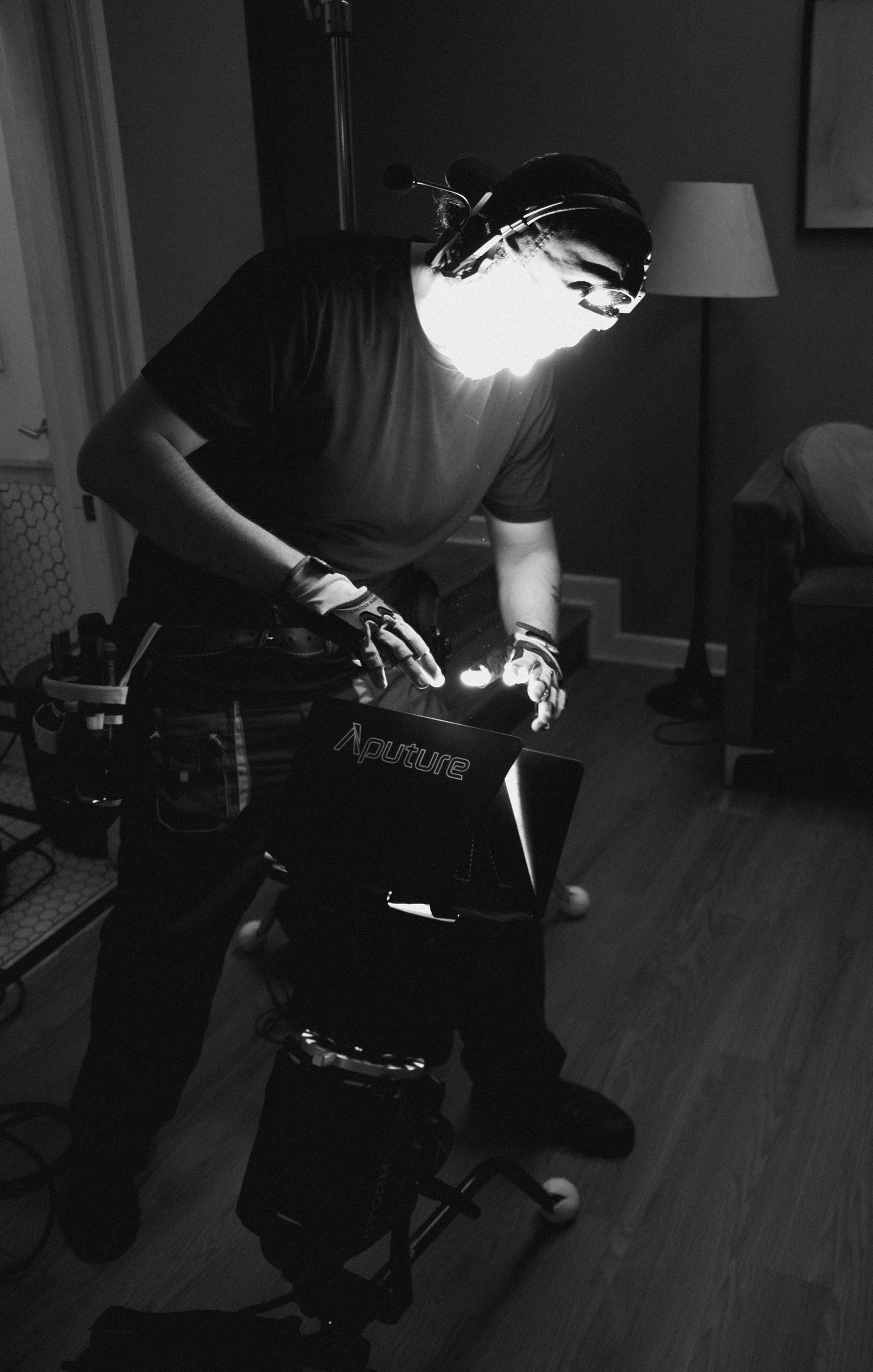 Black and white photo of filmmaker adjusting Aputure light equipment in a dimly lit room.