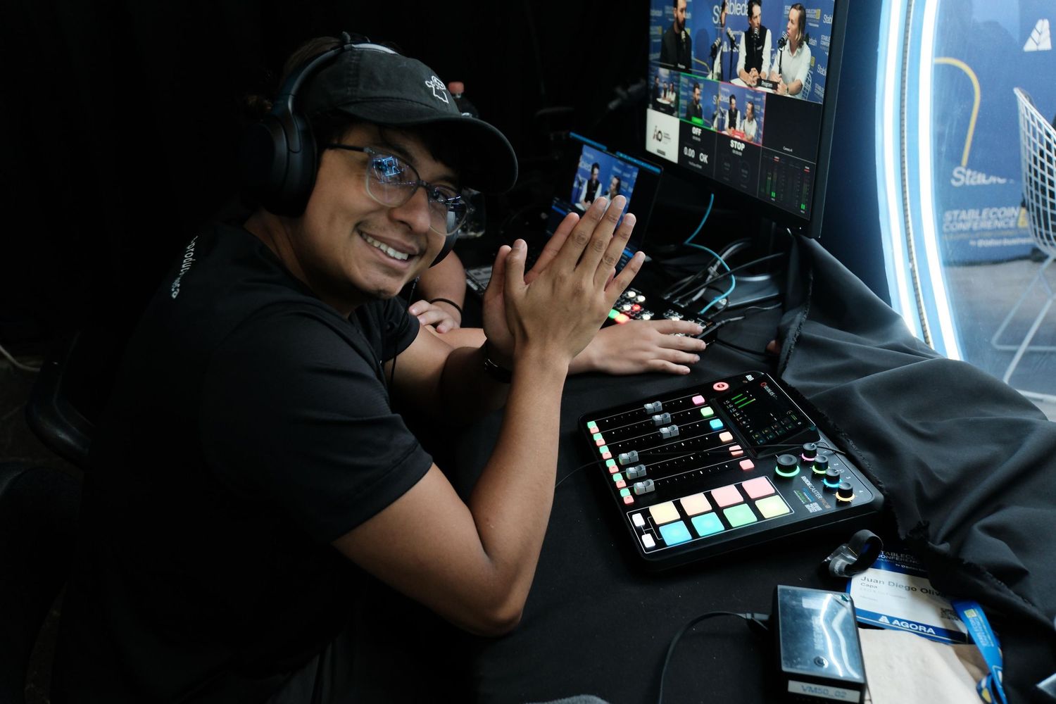 Smiling man with headphones at mixing console clapping hands in dark studio.