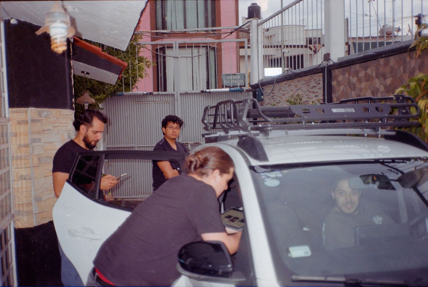 Film crew members working together to mount camera equipment on top of a silver car outdoors.