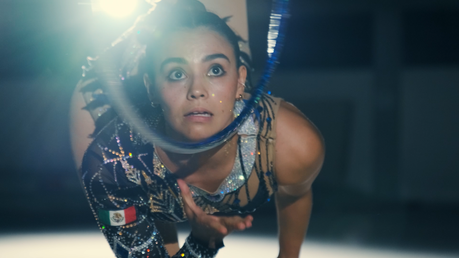 Close-up of focused female gymnast in decorated leotard holding hoop during competition performance.