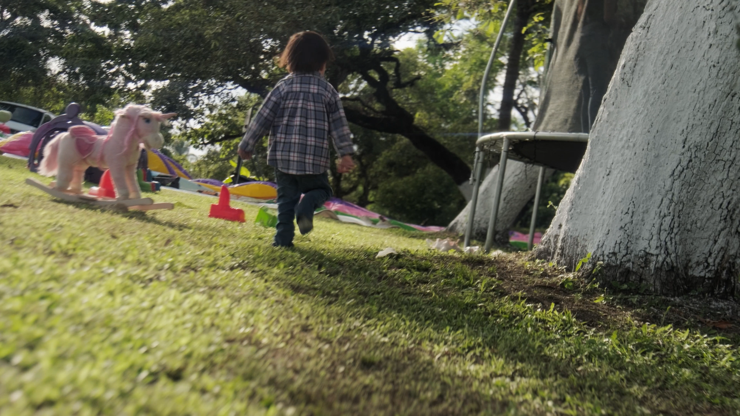 Young toddler runs across green grass in a sunny backyard with colorful toys and a pink rocking horse.