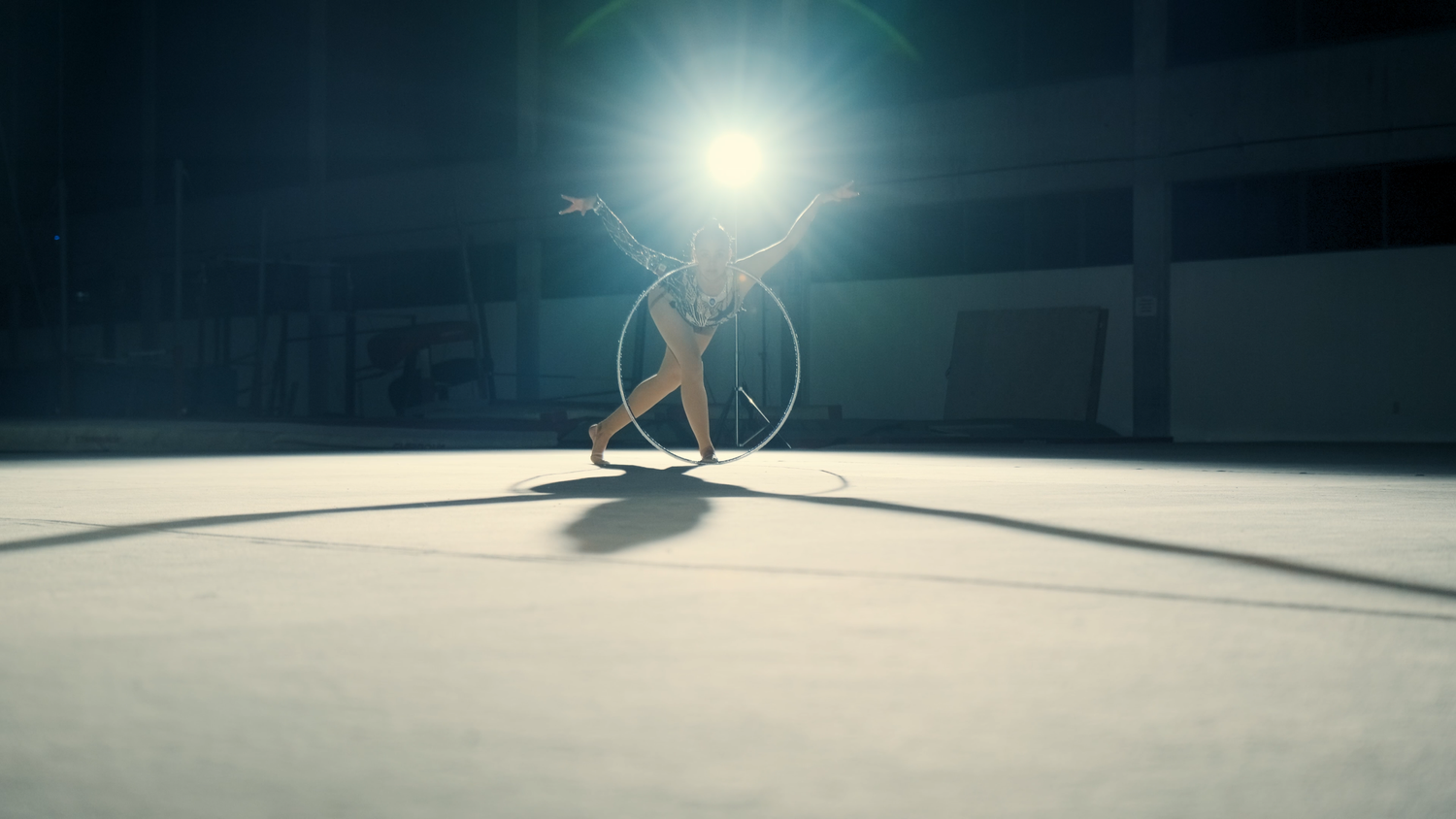 Rhythmic gymnast performing with a hoop under dramatic spotlight on a competition floor.