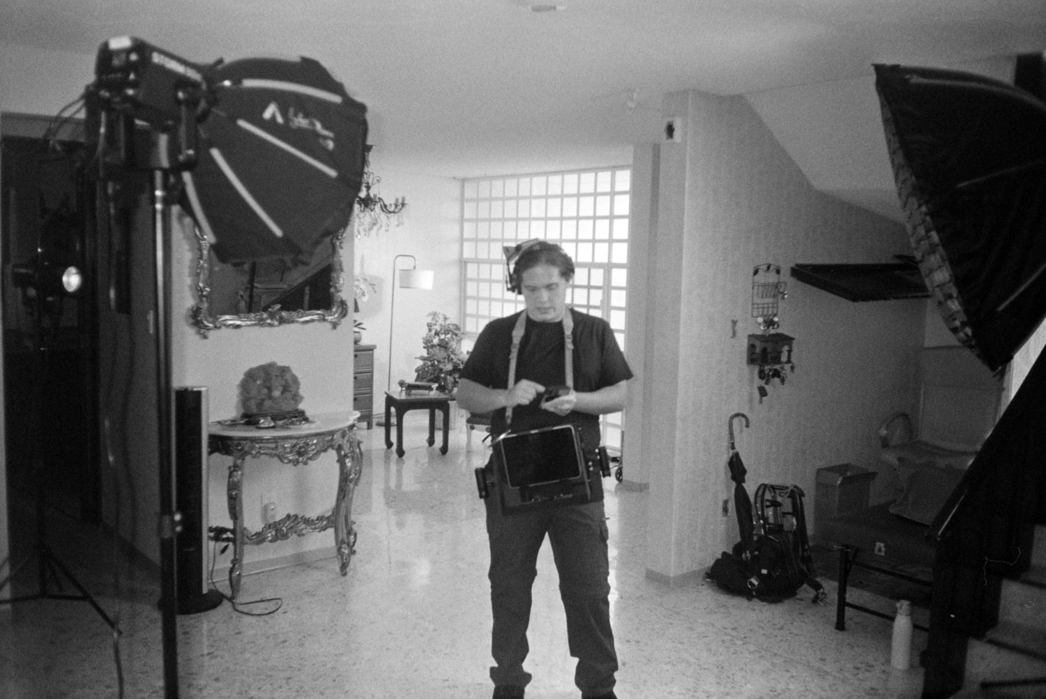 Black and white photo of filmmaker standing between professional lighting equipment in a home interior.