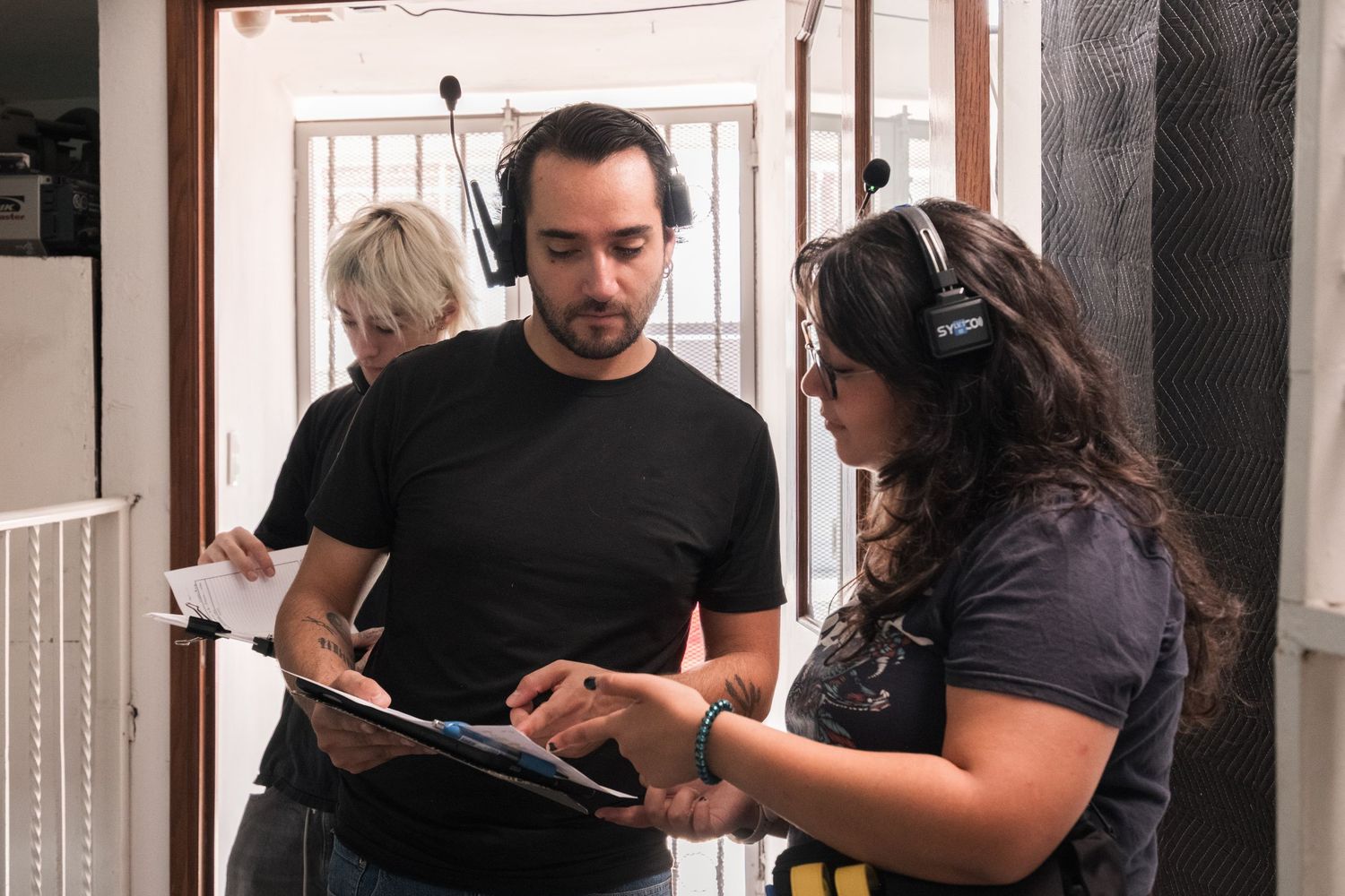 A man and woman reviewing scripts with headphones on a film production set.