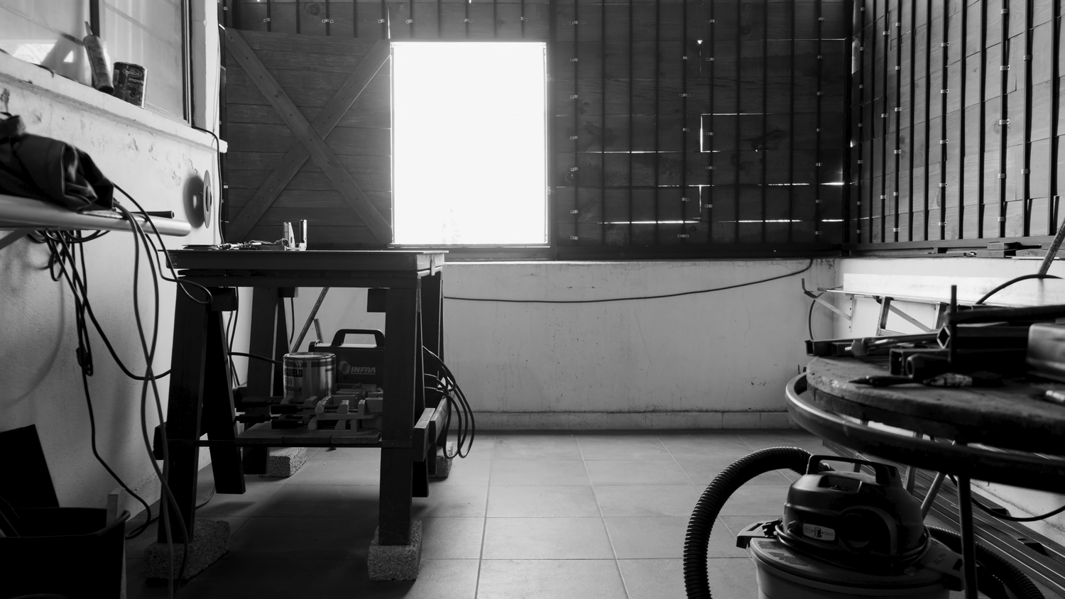 Black and white photo of industrial workspace with metal table and equipment under bright window.