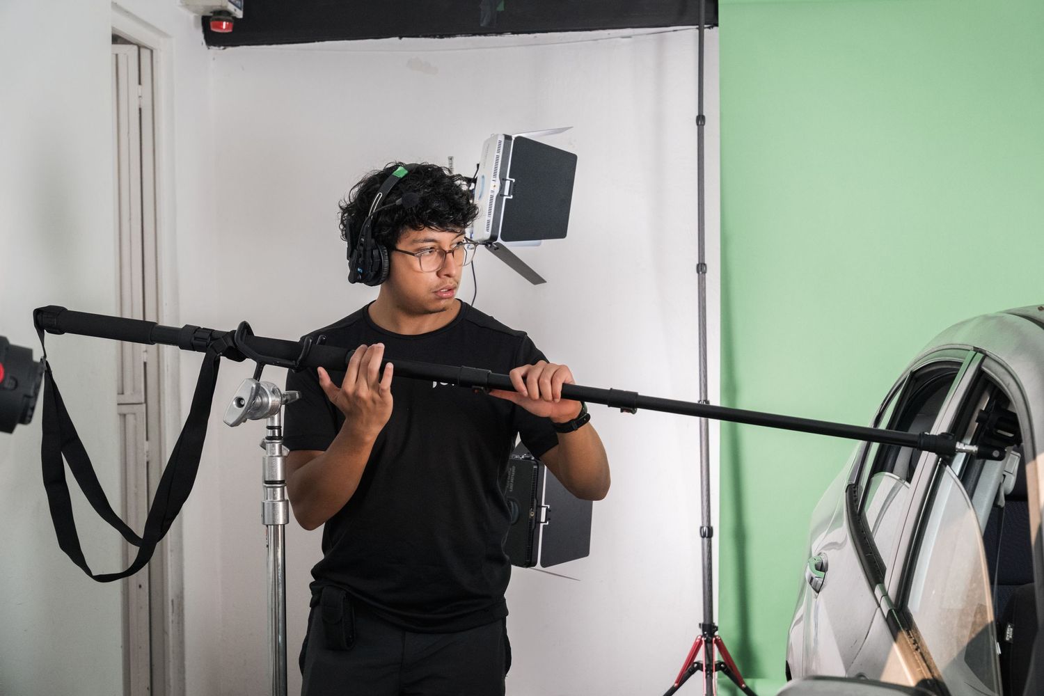 A sound technician holds a boom microphone pole on a green screen film production set.