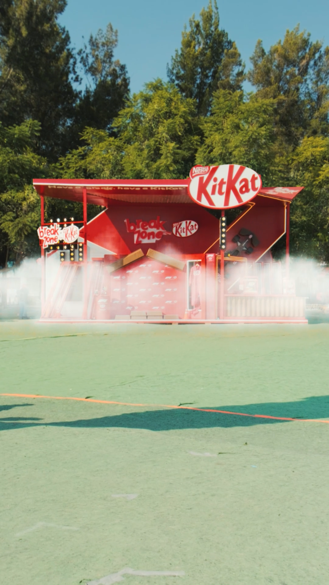 Red KitKat branded promotional booth with smoke effects on an outdoor sports court.