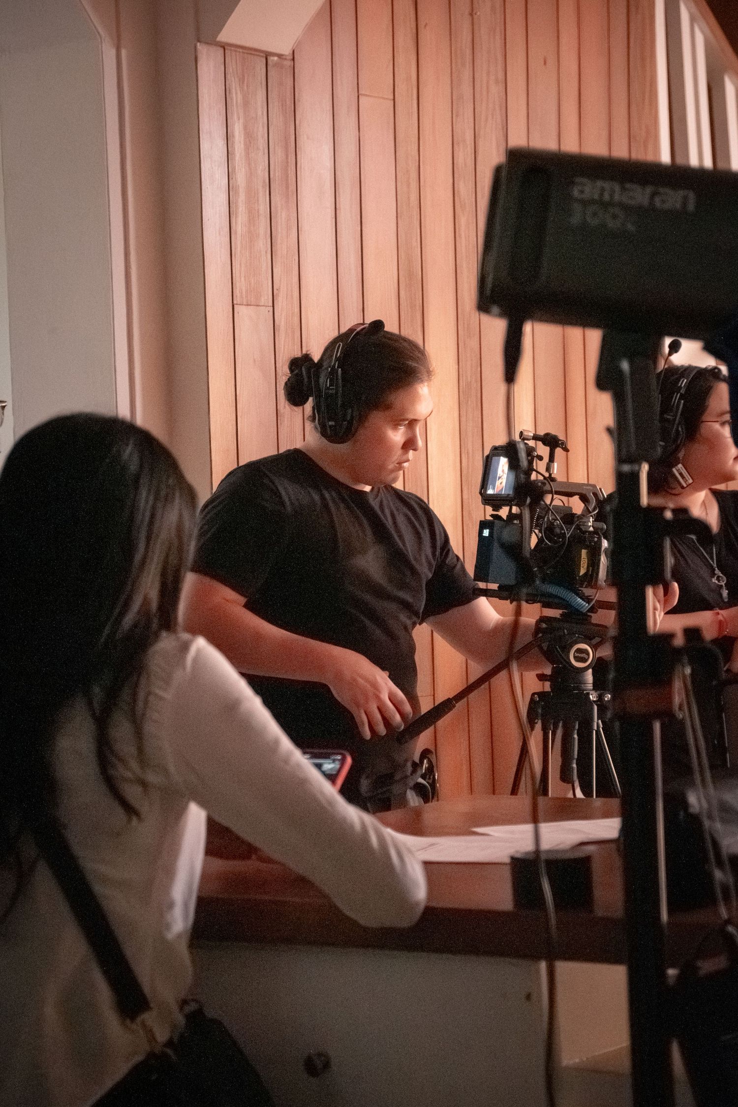 Film crew members wearing headphones operate a camera on set with professional lighting equipment.