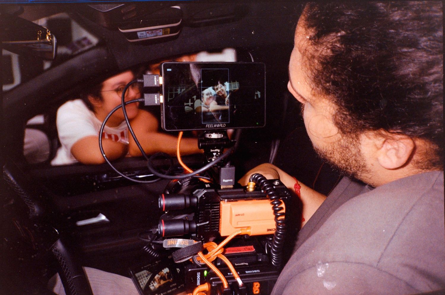 Filmmaker operating professional camera equipment inside a car during a film production shoot.