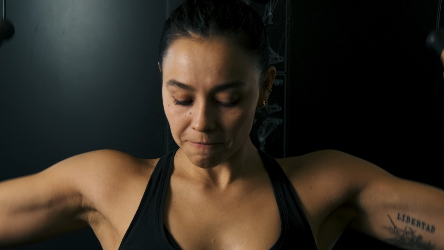 Female athlete in black sports bra resting after intense gym workout in dark studio.