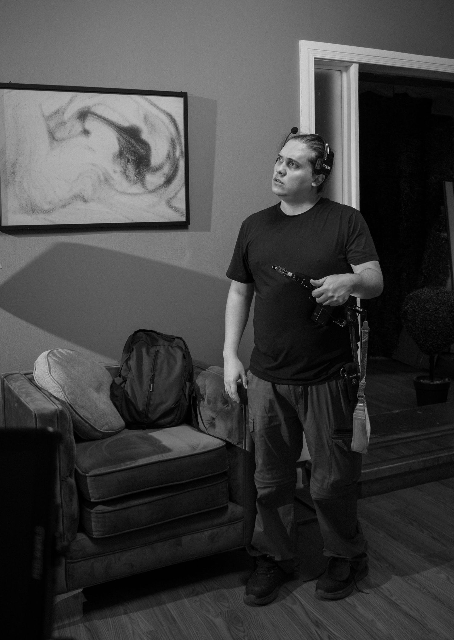 Black and white photo of a film crew member holding equipment while standing in a dimly lit room.