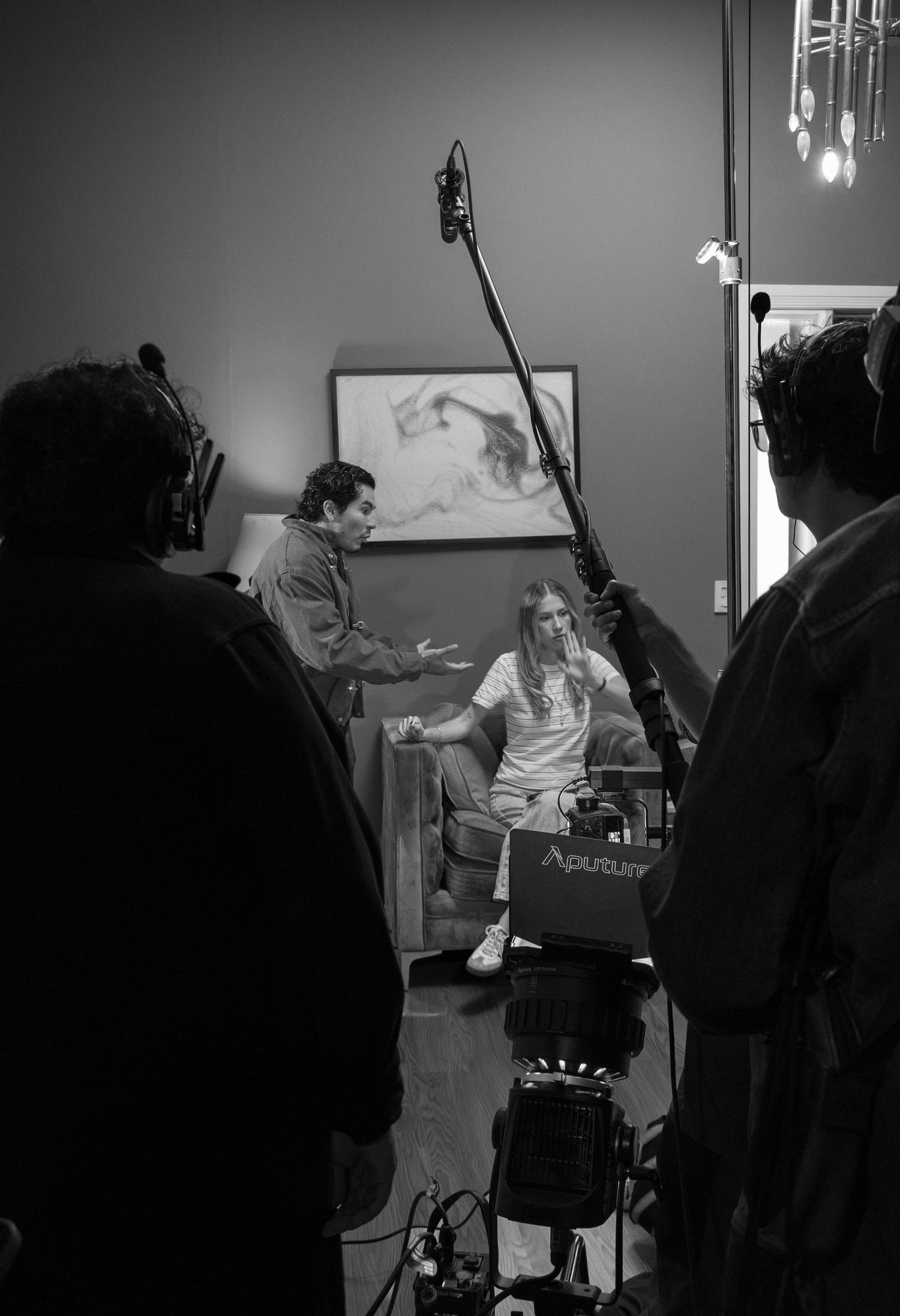 Black and white BTS photo of film crew directing actress seated in chair with boom mic overhead.