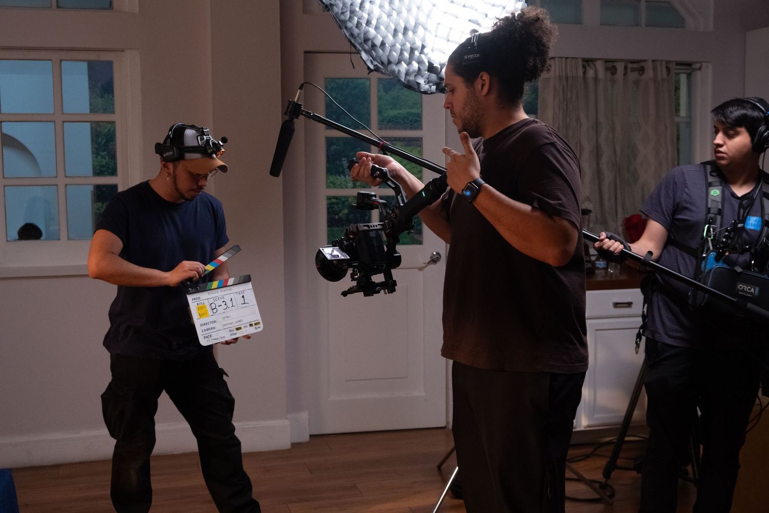 Film crew with camera and clapperboard shooting scene in bright indoor location.