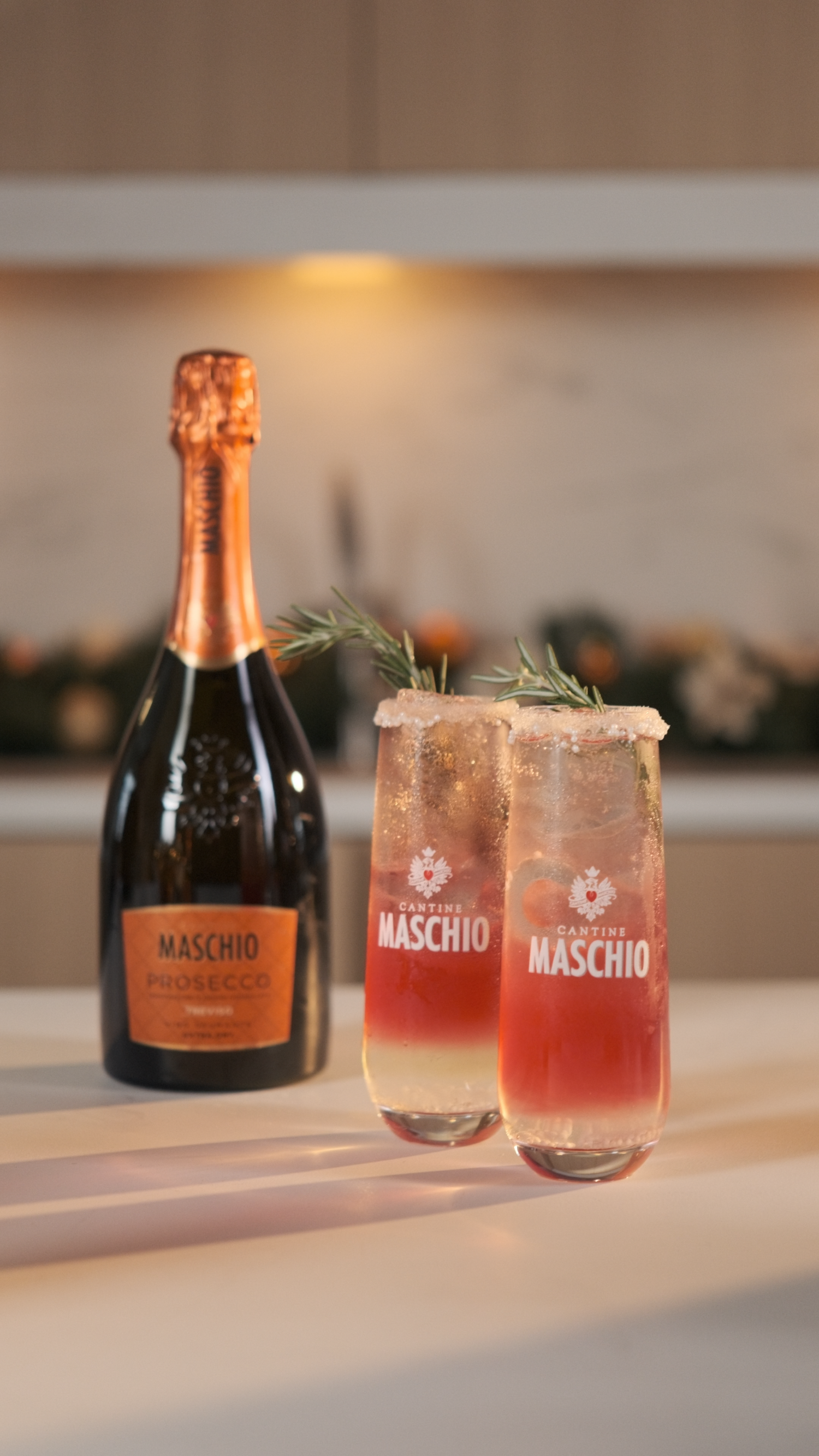 Two Maschio Prosecco cocktails garnished with rosemary beside a bottle of Maschio Prosecco on a marble counter.