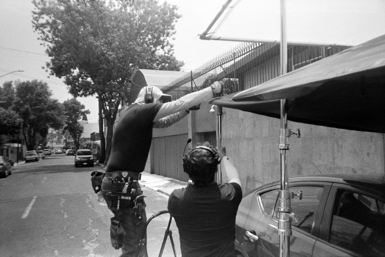Two crew members set up equipment on a sunny street during a film production shoot.
