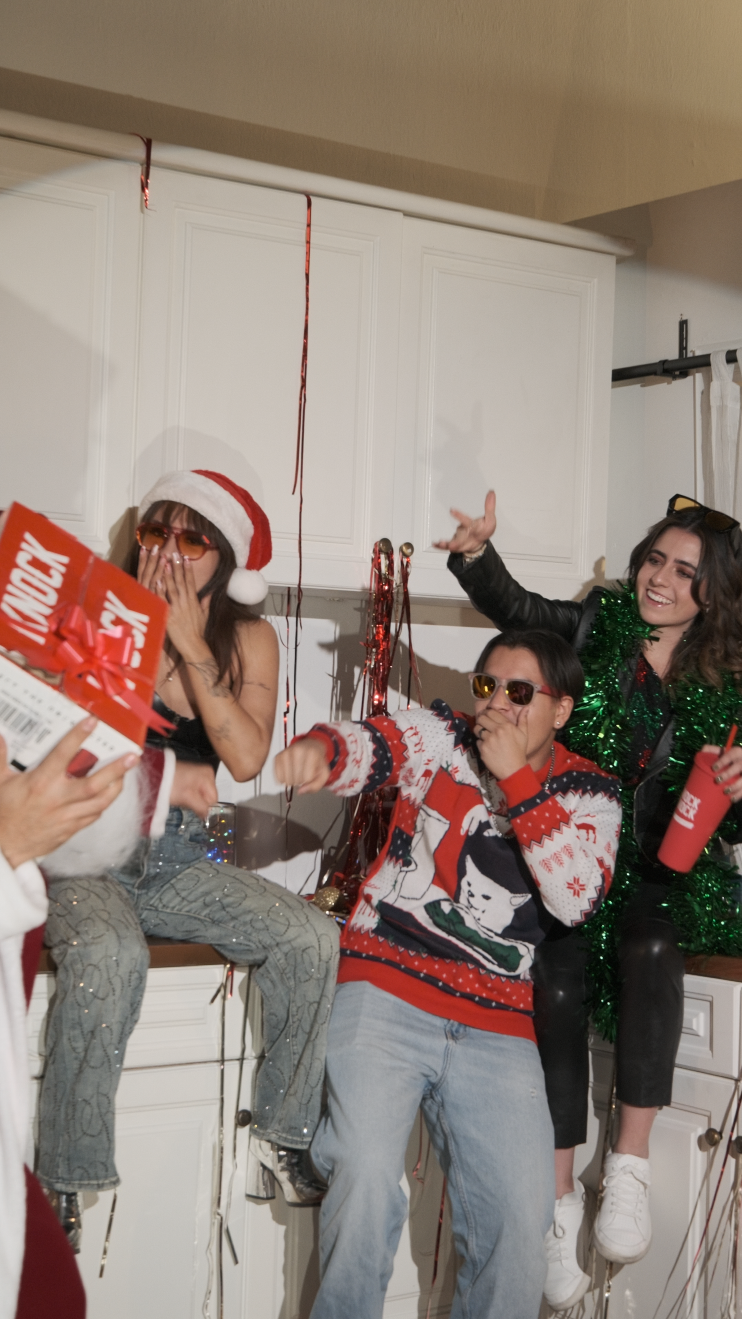 Friends celebrating at Christmas party with Knock Knock wine gift box, Santa hat, and holiday streamers.