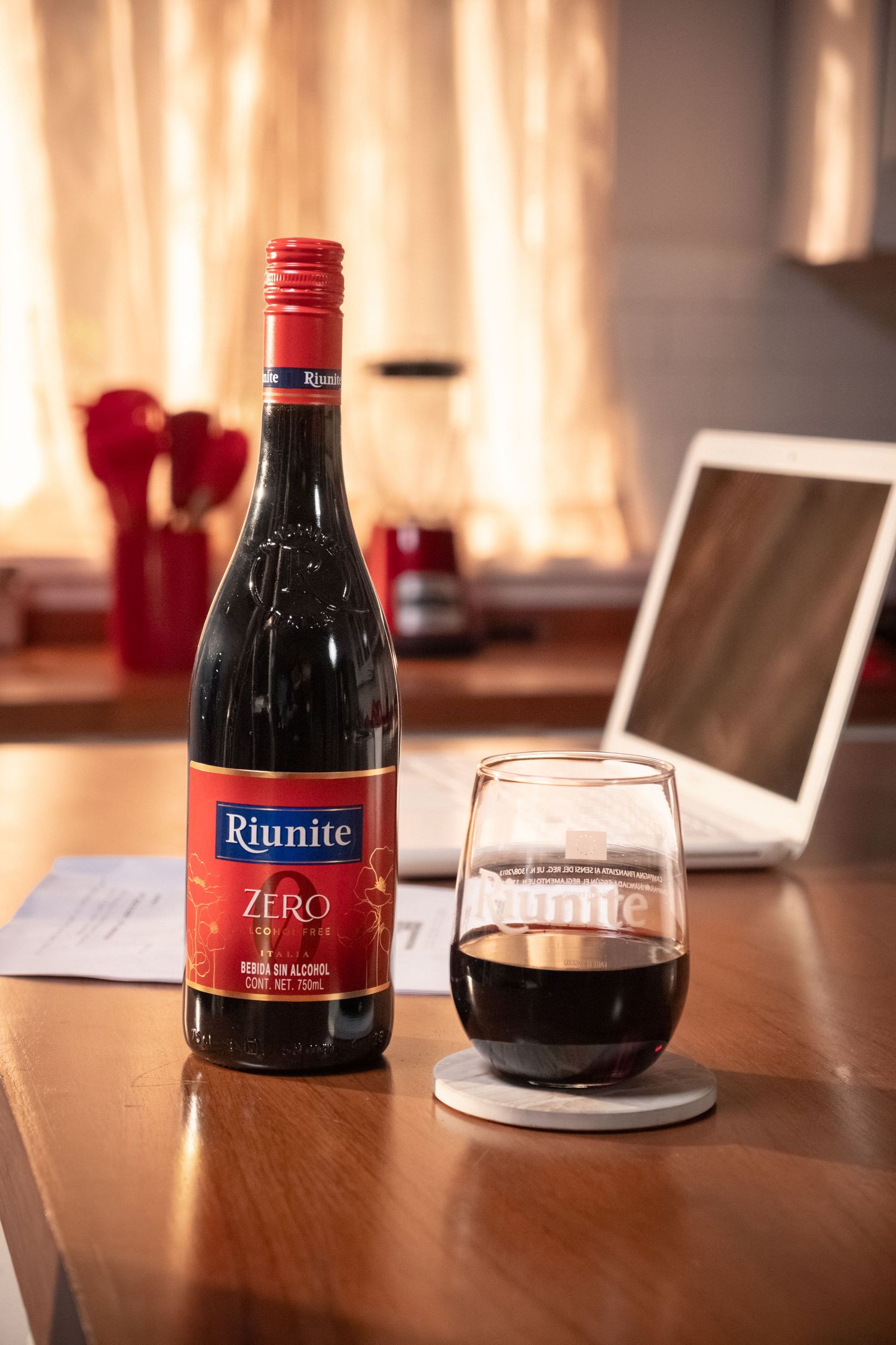 Riunite Zero non-alcoholic red wine bottle and glass on wooden table.
