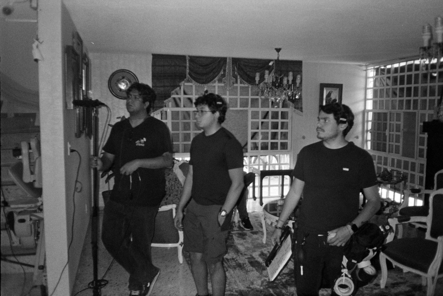 Black and white photo of three crew members standing in a home interior during film production.