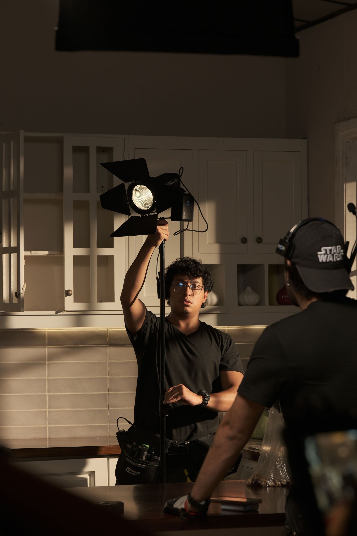 Film crew member adjusting a professional light on set in a kitchen environment during production.