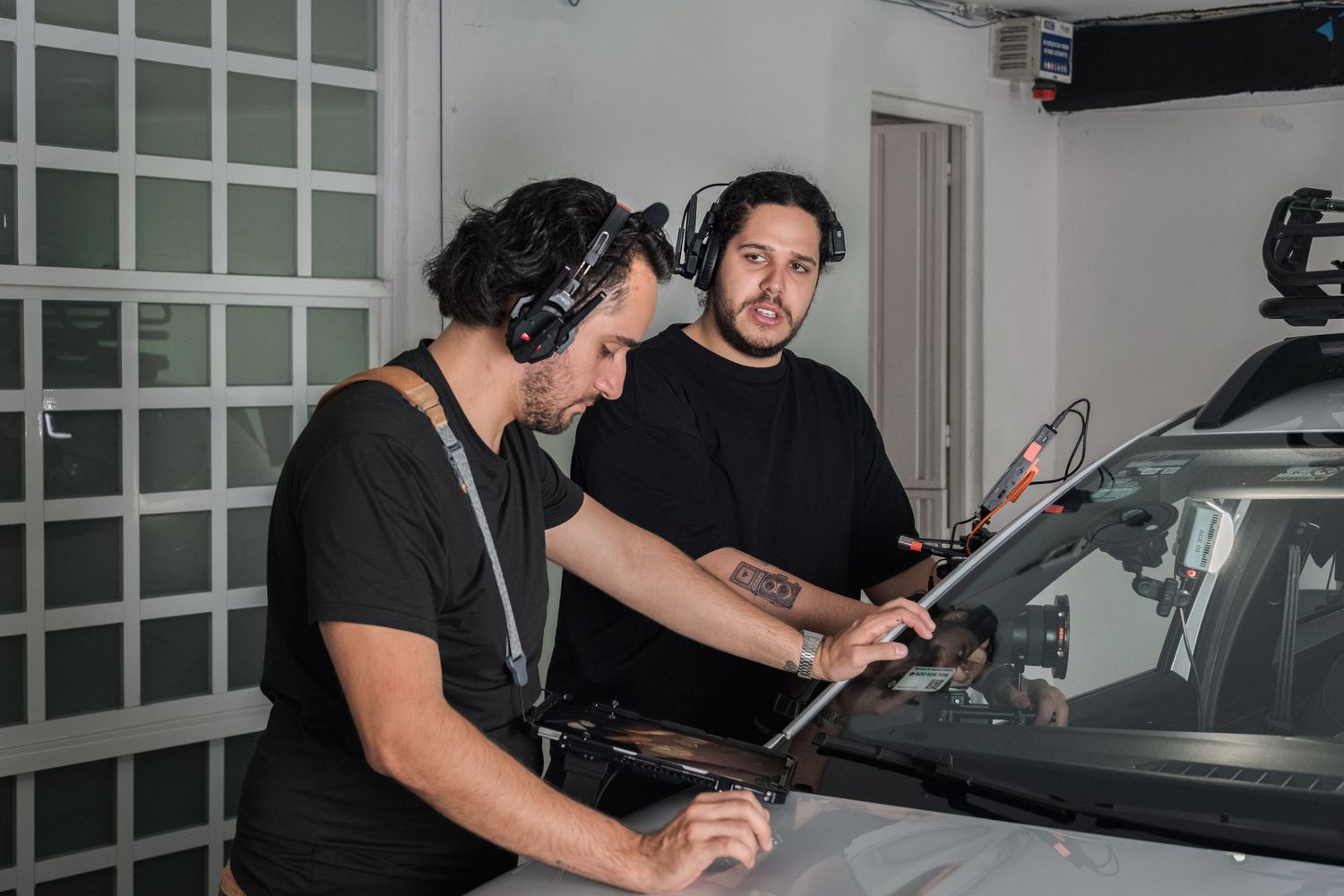 Two film crew members in headphones working on a car windshield on set.