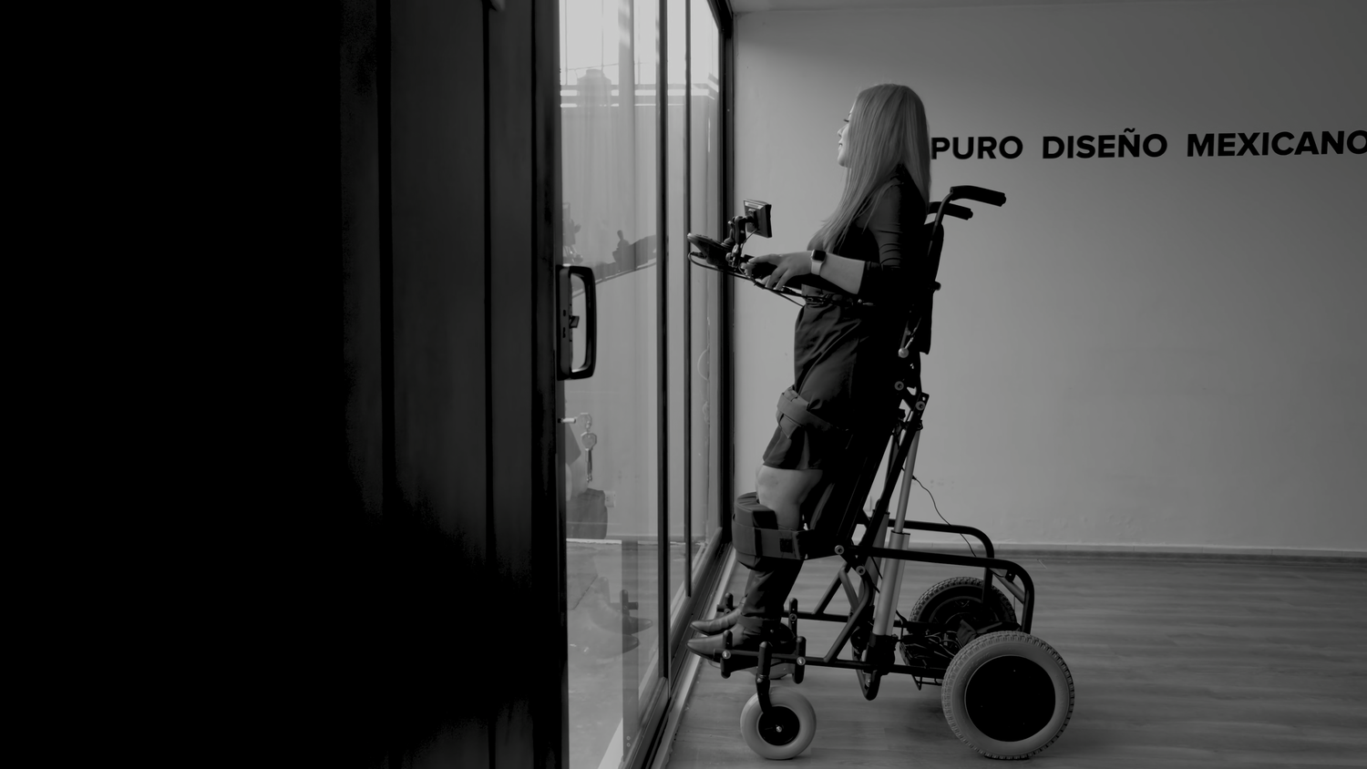 Black and white photo of person with wheelchair near glass door with Puro Diseno Mexicano sign.