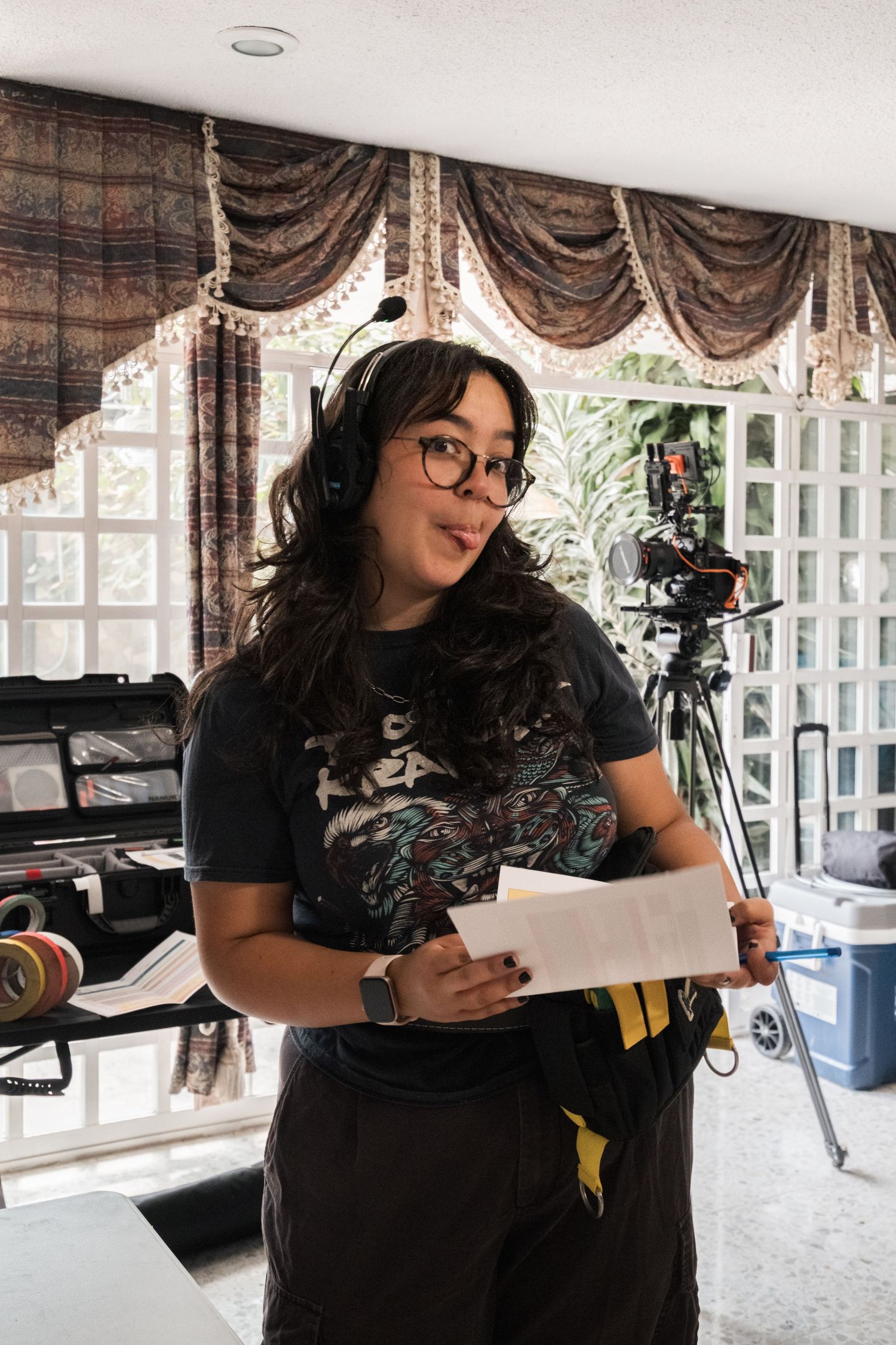 Female film director wearing headphones holds script on indoor movie production set.