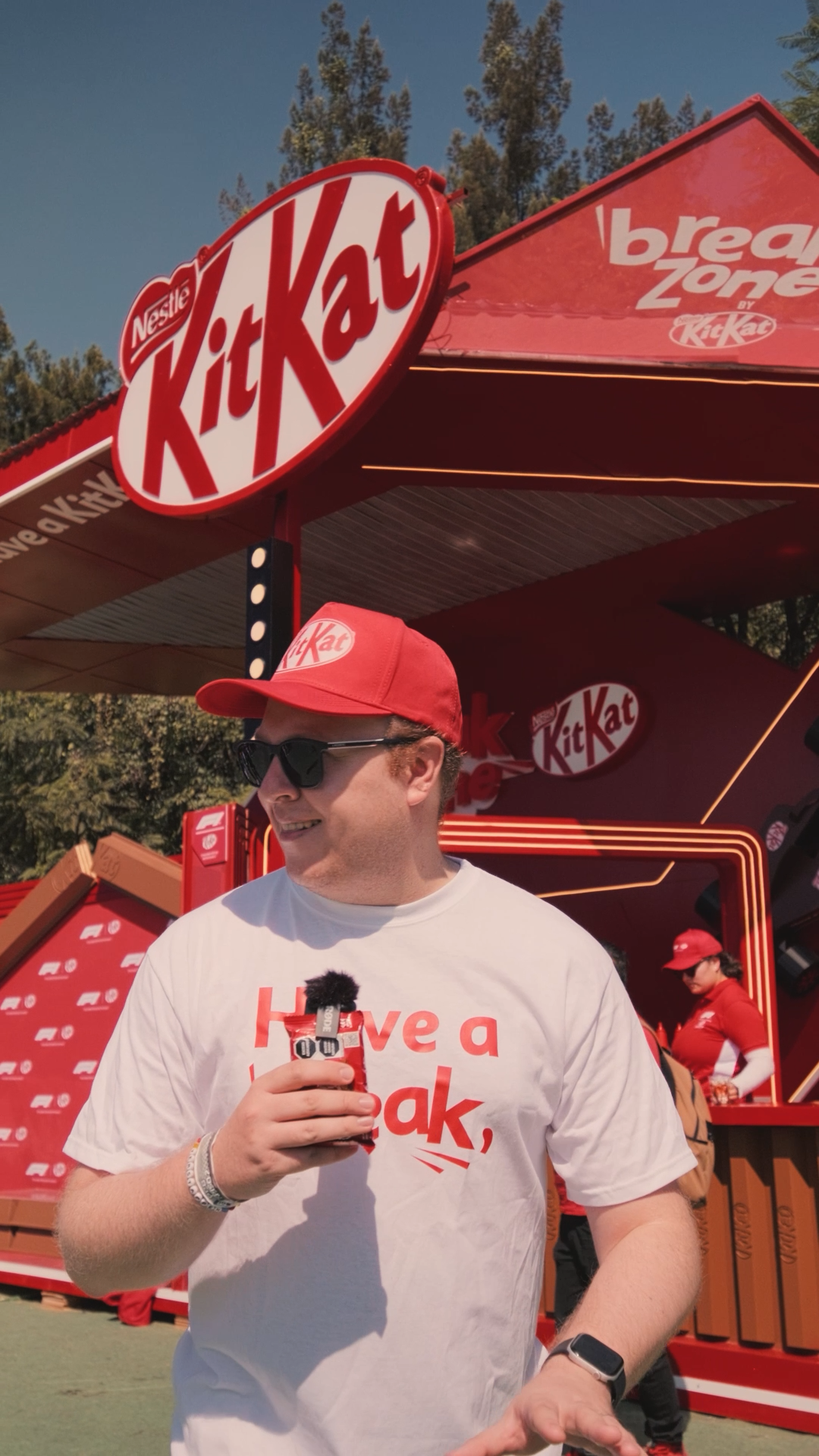 Man wearing KitKat Have a Break t-shirt and red cap holding drink at KitKat Break Zone promotional booth.