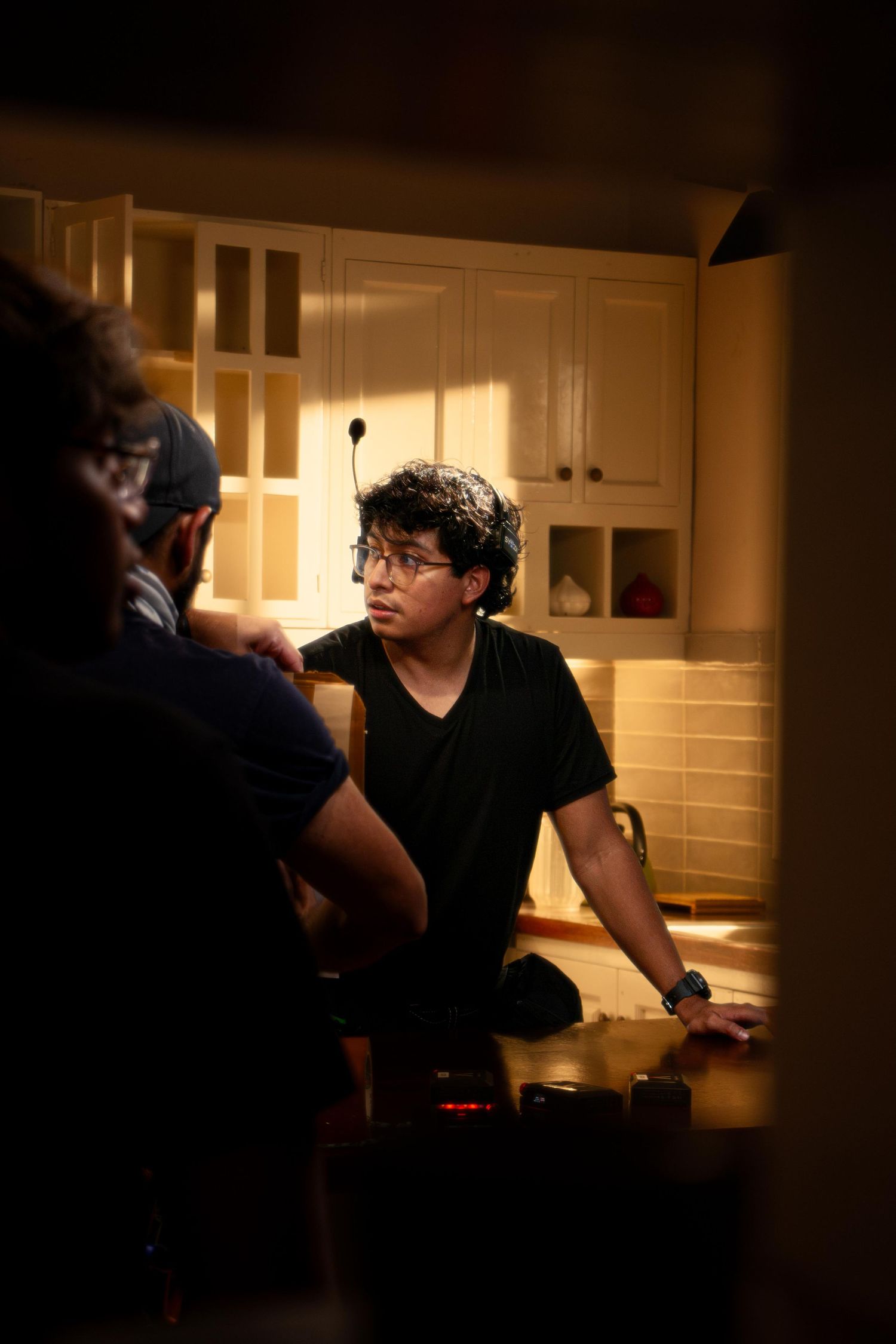 Young filmmaker in glasses and black t-shirt sits at kitchen table during film production meeting.