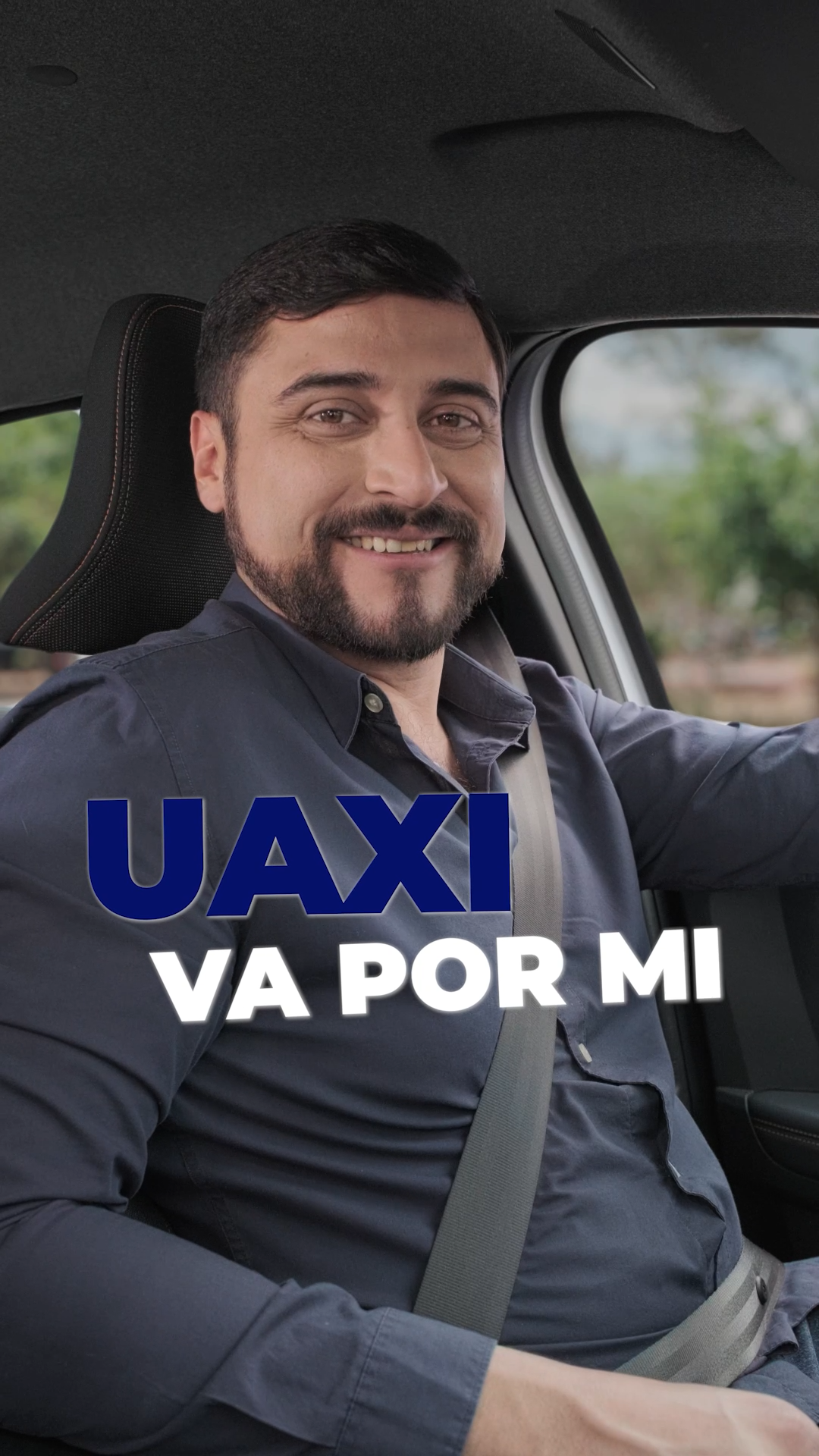 Smiling bearded man in a car with UAXI VA POR MI text overlay promoting a ride-sharing service.