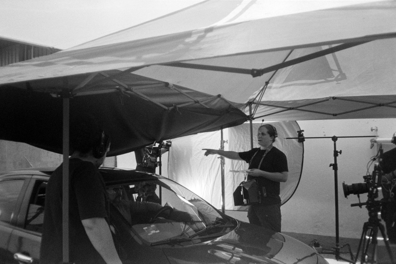 Black and white behind scenes photo of film crew directing car scene under canopy.