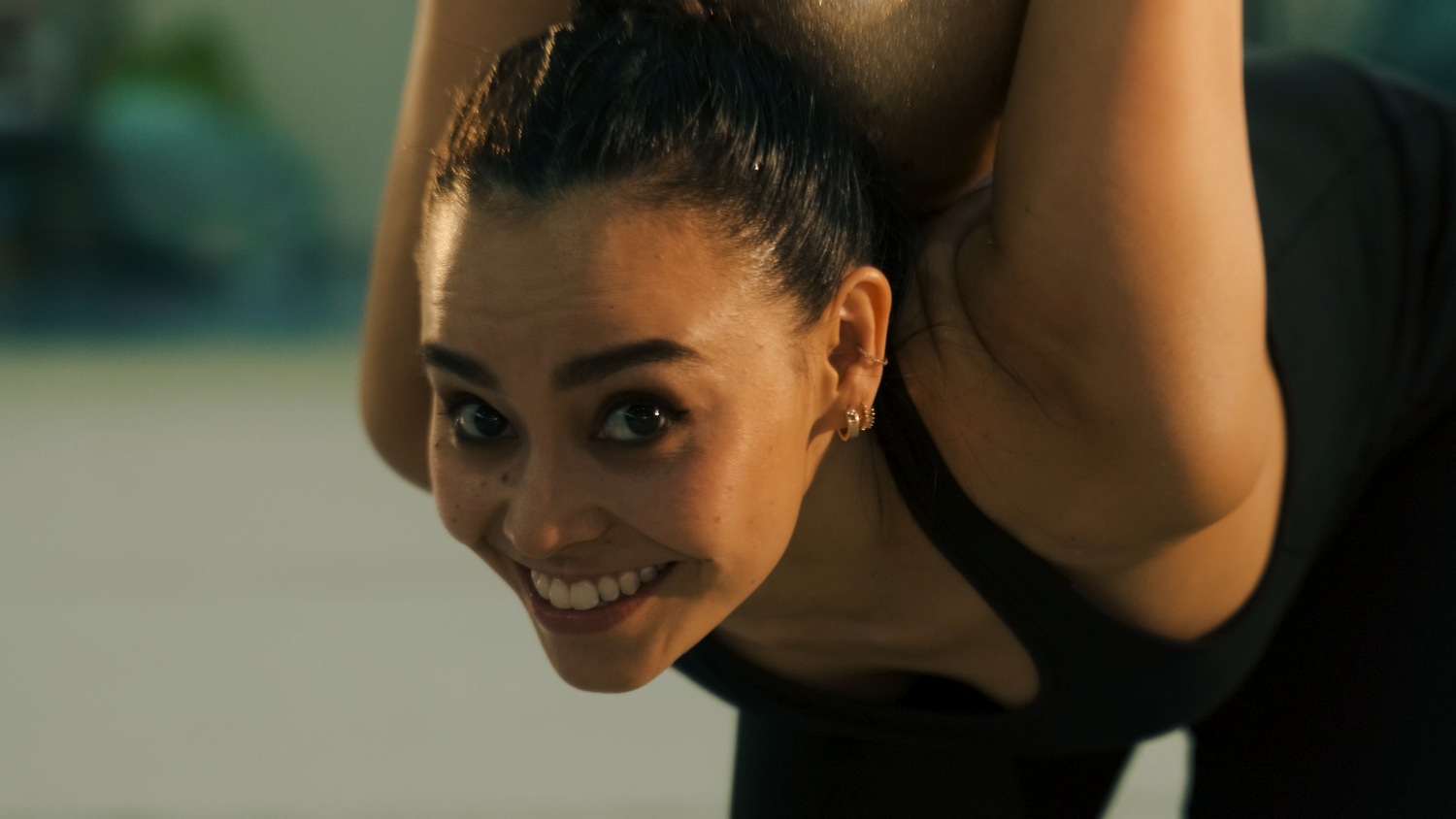 Smiling female gymnast in black leotard stretching during training session.