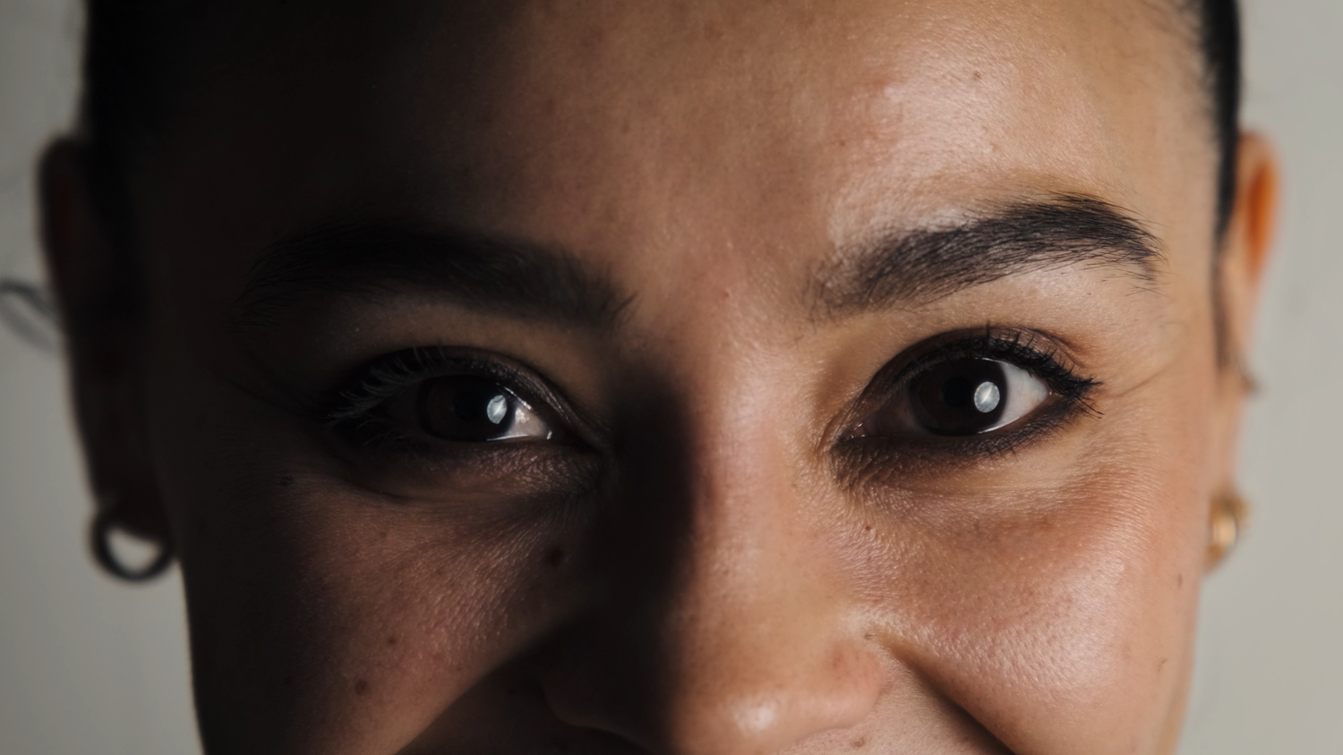 Close-up portrait of a woman with dark eyes, bold eyebrows, and glowing skin smiling softly.