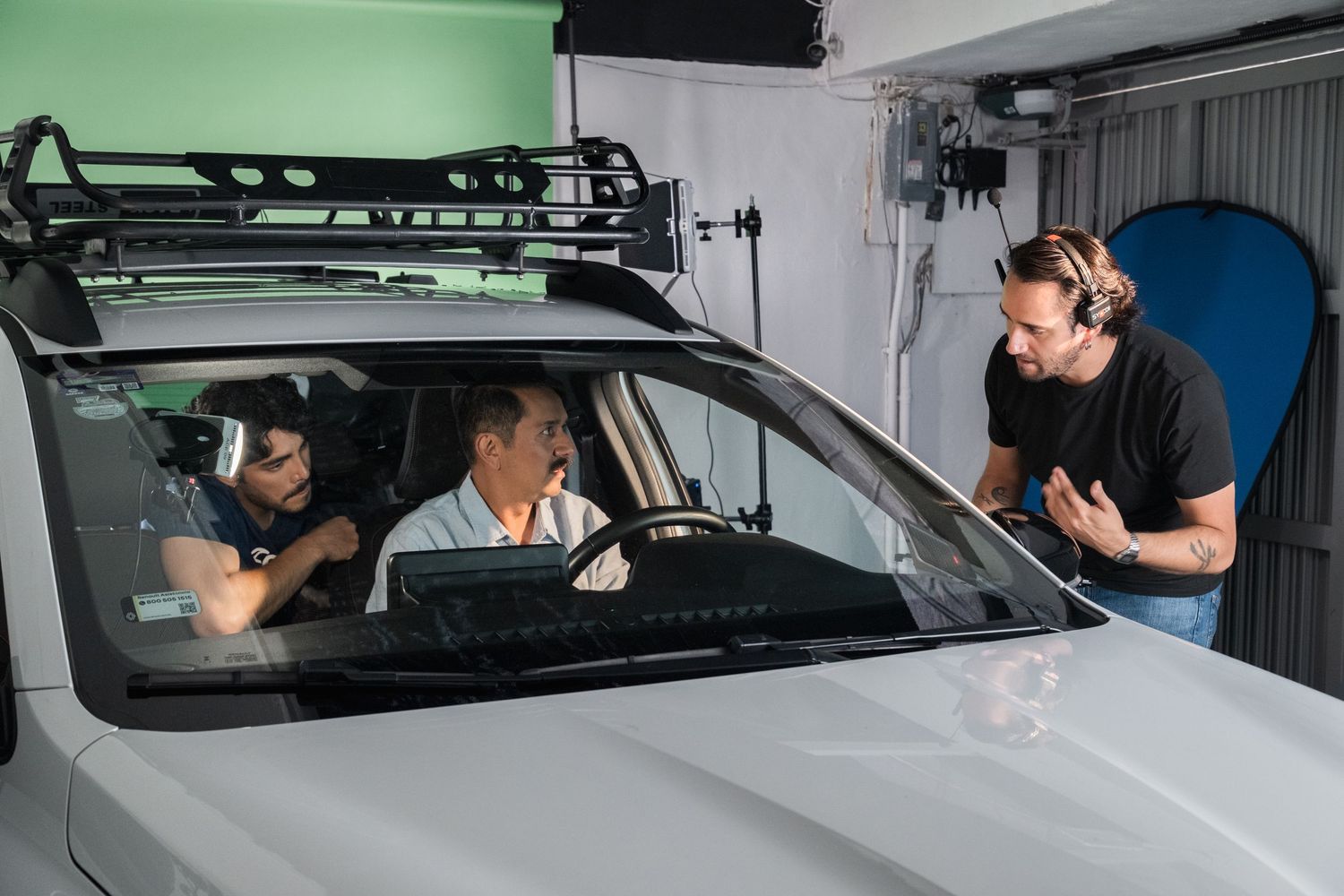 Director discusses scene with two actors seated in car on green screen studio set.