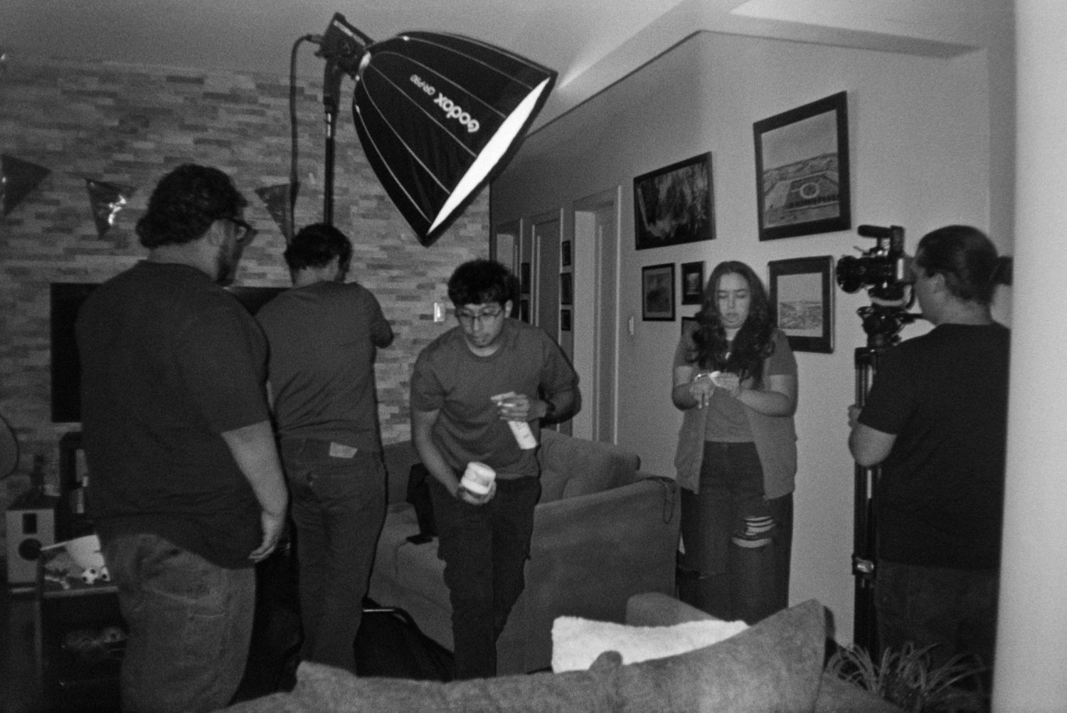 Film crew records a scene in a living room with professional lighting and camera equipment.
