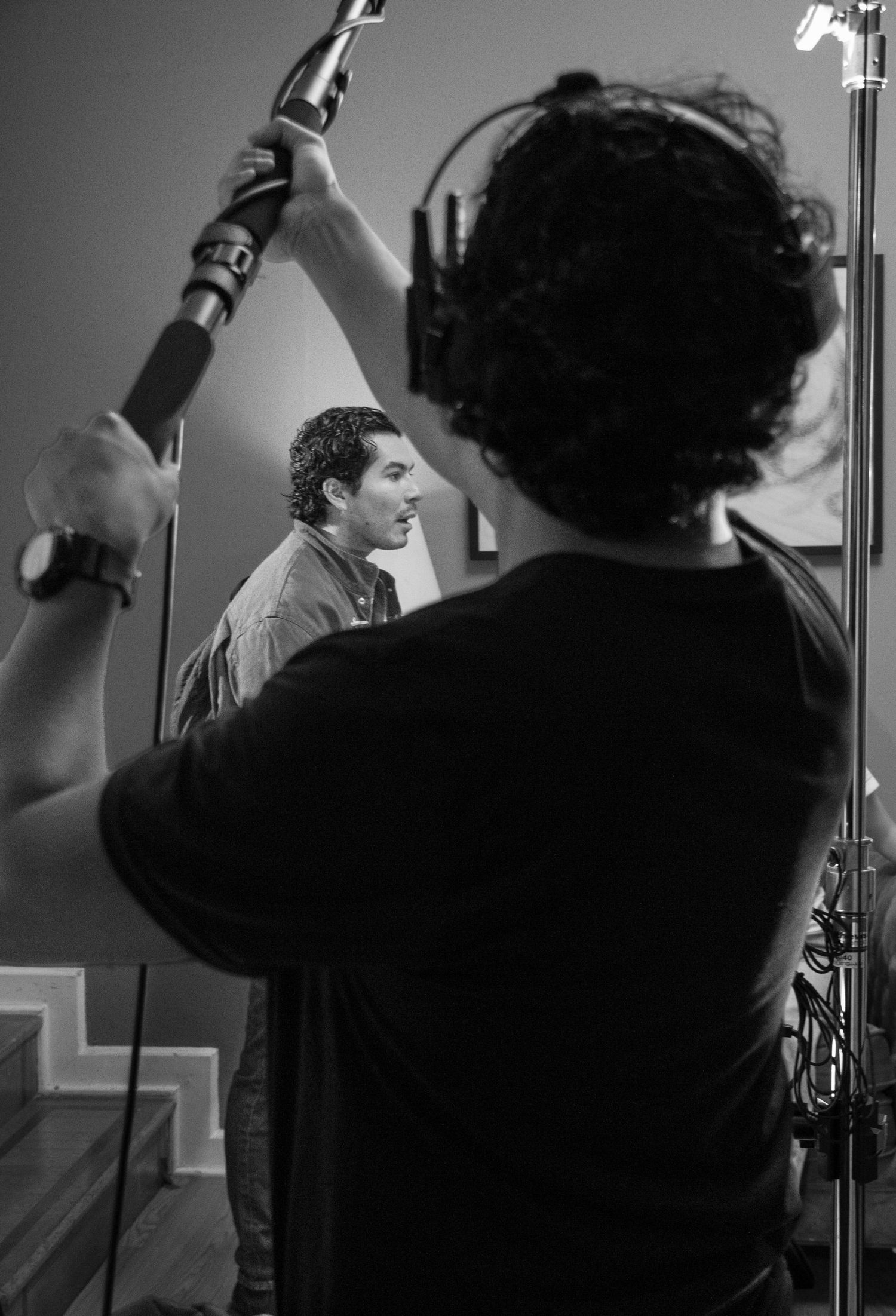 Behind-the-scenes boom mic operator holds microphone overhead during film production shoot in black and white.
