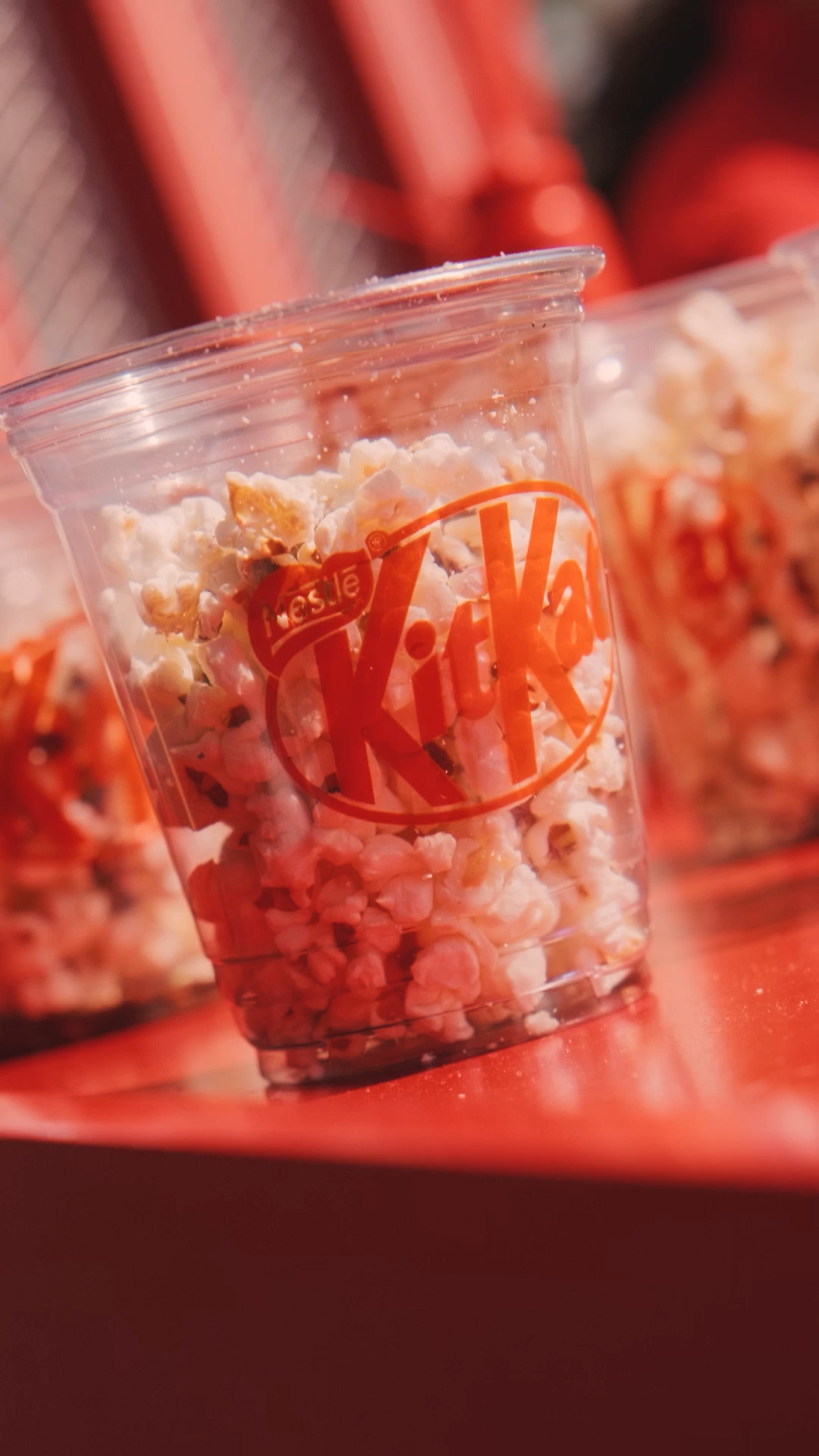 Clear plastic cup branded with KitKat logo filled with popcorn and chocolate pieces at a Nestle event.
