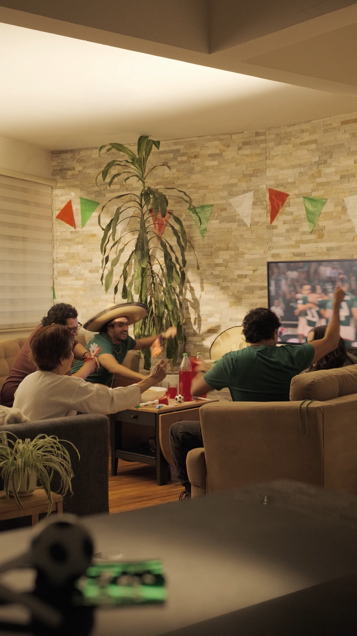 Friends watching sports on TV in cozy living room with Mexican flag bunting decor.