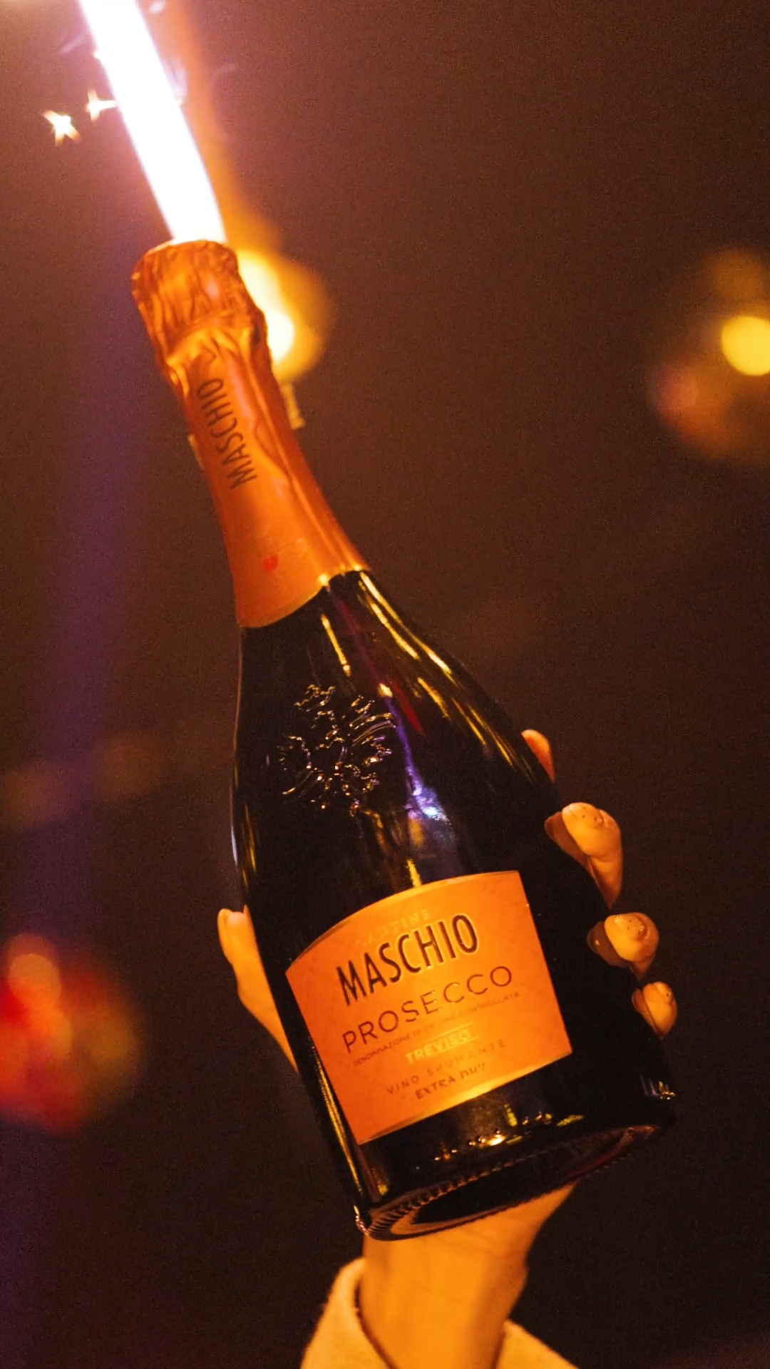 Hand holding Maschio Prosecco bottle with sparkler firework at celebration party event.